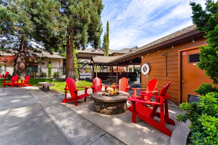 Outdoor patio with red Adirondack chairs around a stone fire pit beside a wooden building