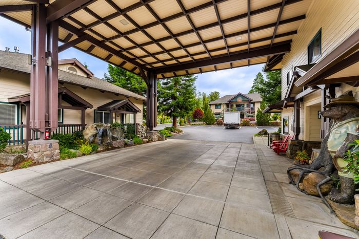 Covered driveway at a resort entrance with tiled roofs, stone planters, and buildings in the background