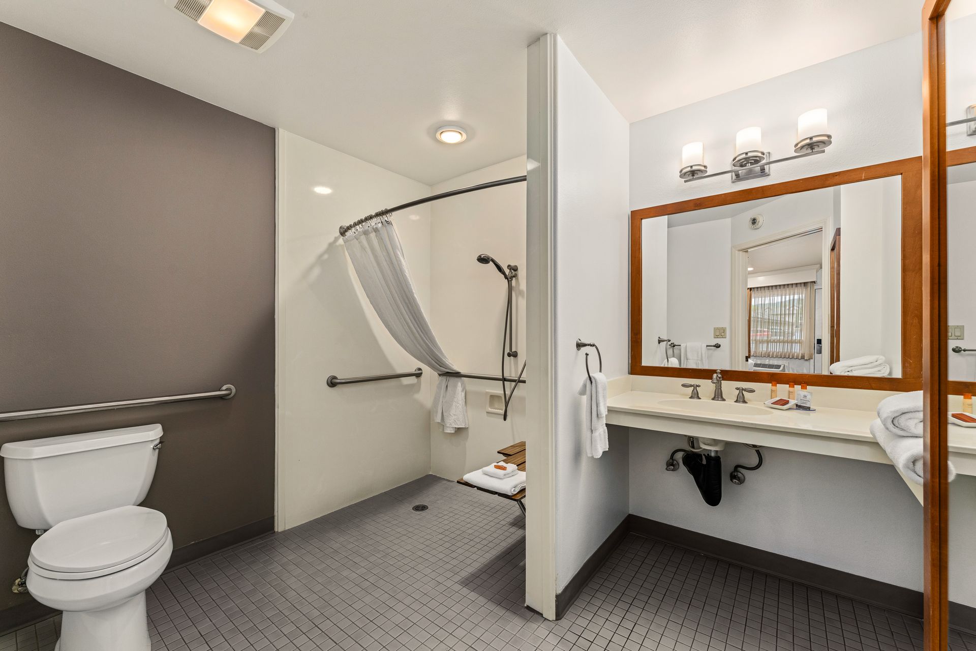 Accessible bathroom with toilet, roll-in shower, sink, and large mirror