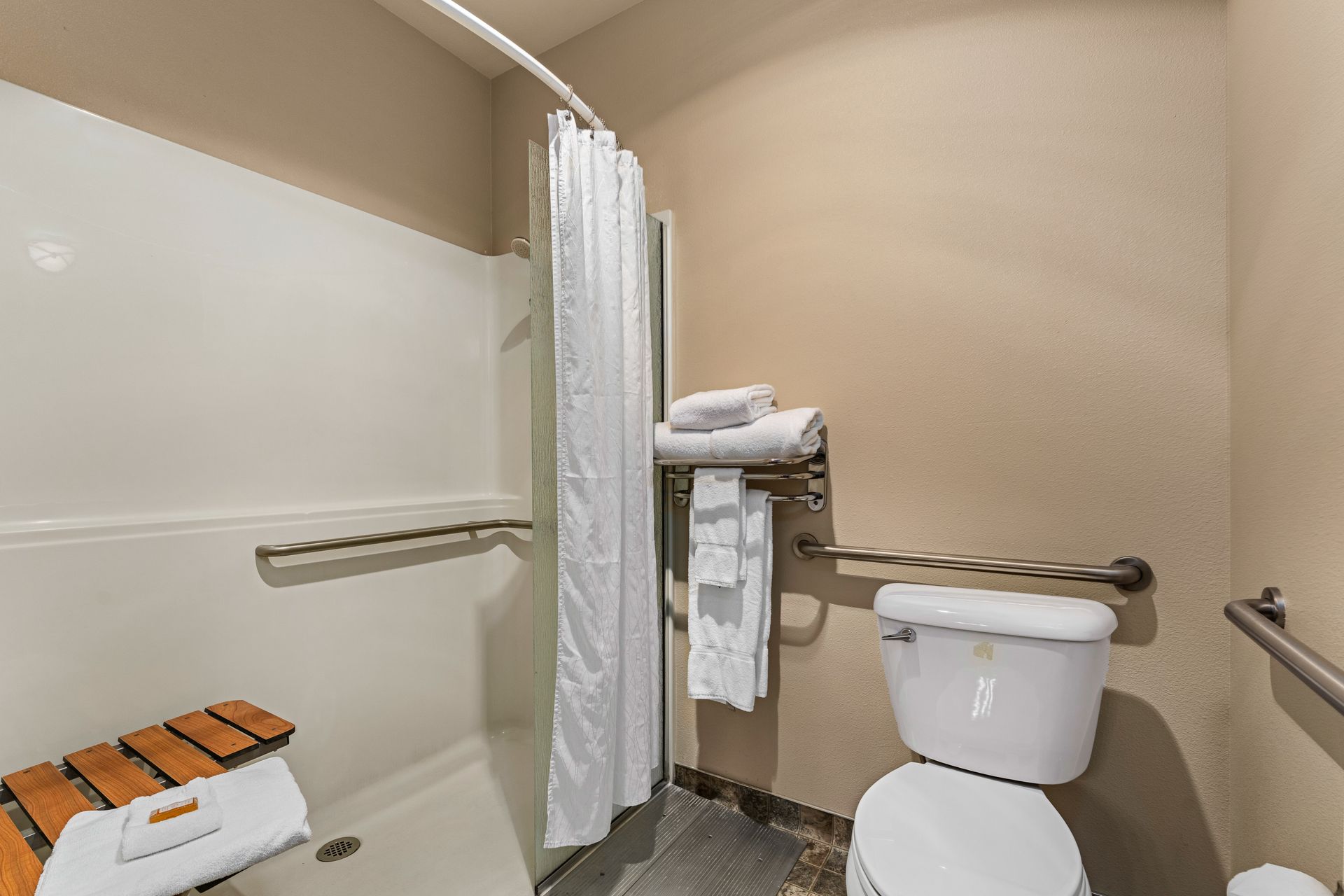 Accessible bathroom with shower curtain, toilet, towel rack, and wall grab bars