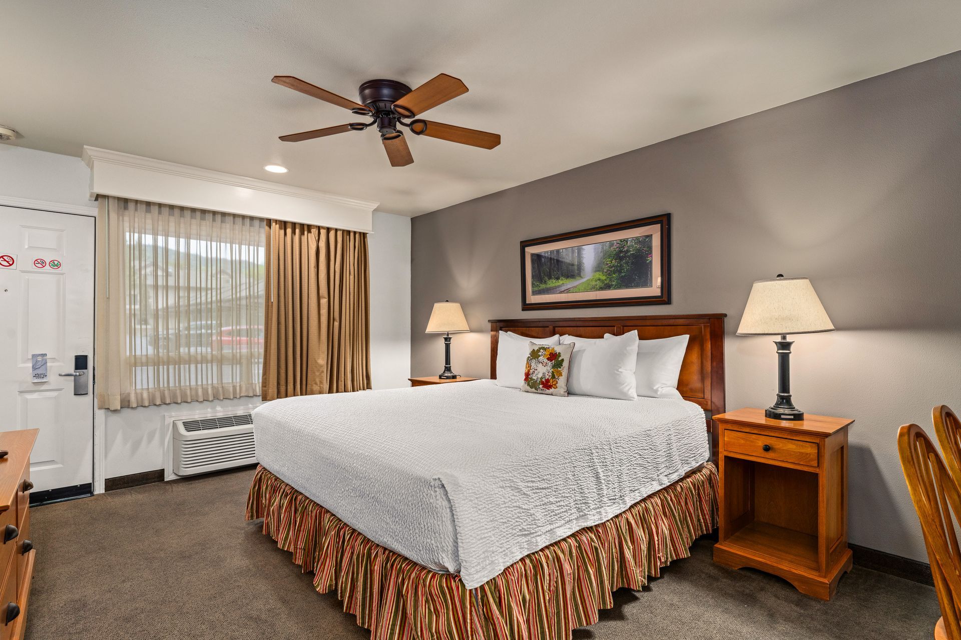 Cozy hotel room with a king bed, nightstands, lamps, ceiling fan, and window with curtains
