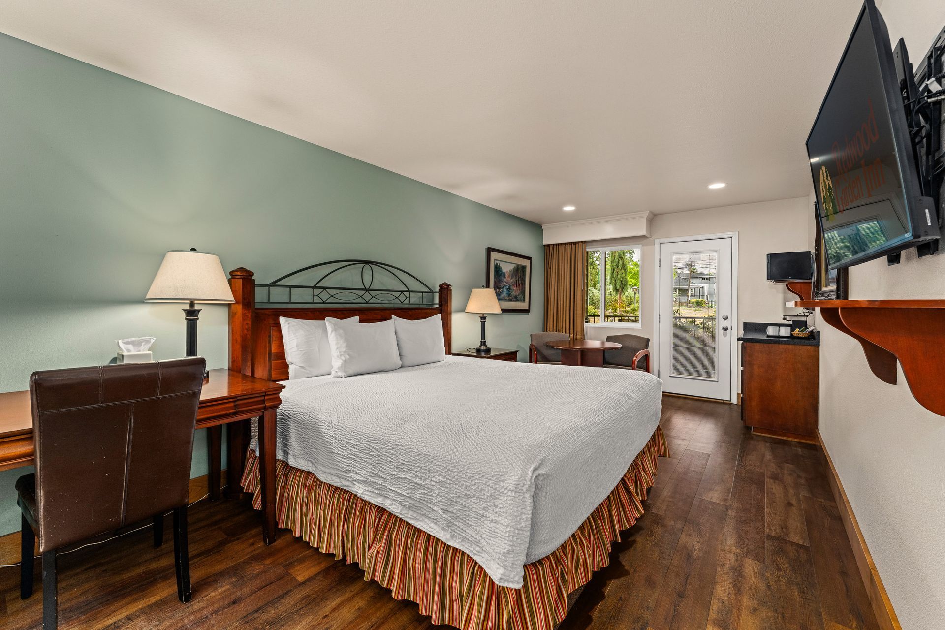 Bedroom with a king bed, desk, TV, and balcony doors in a bright, modern interior