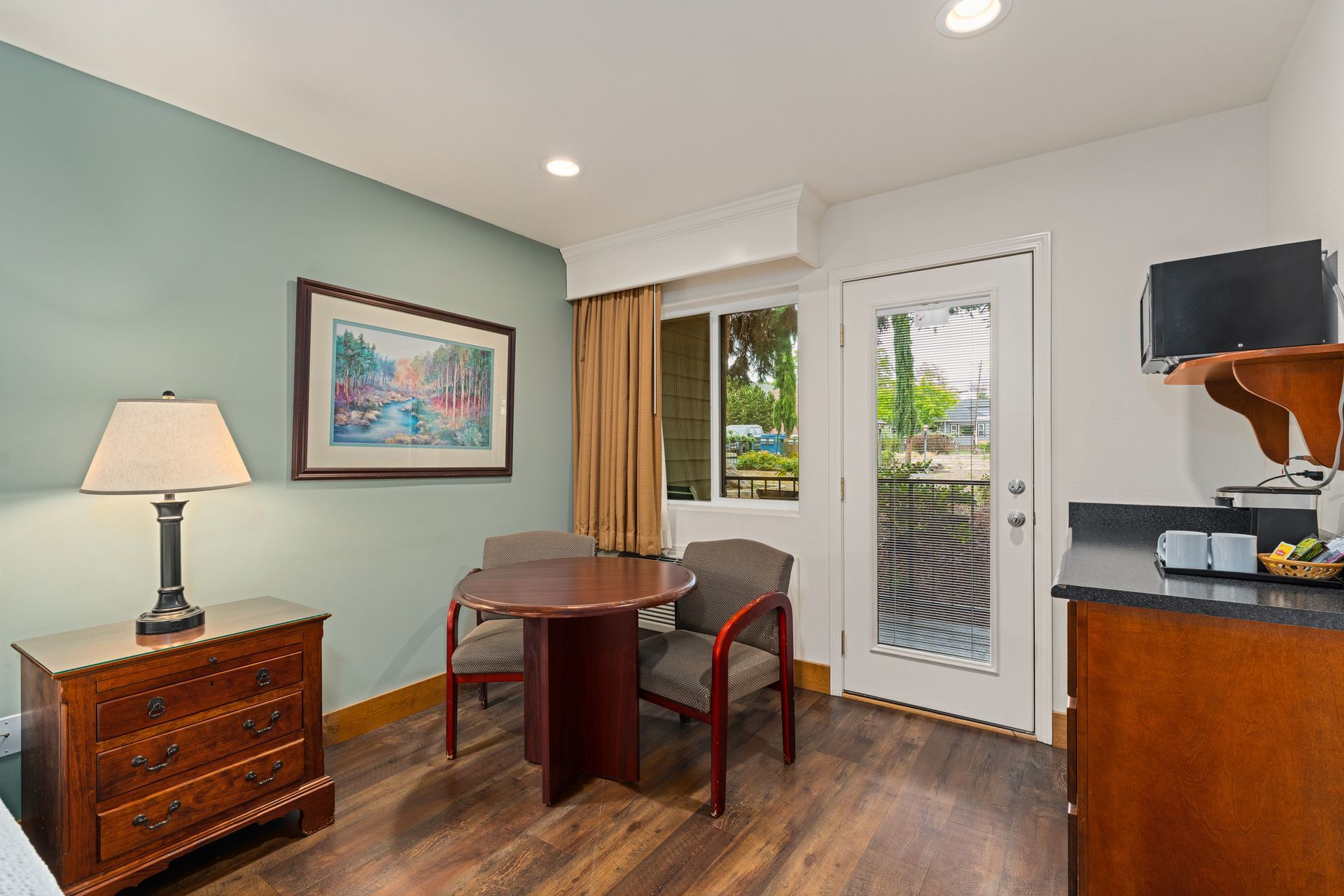 Small office with desk, lamp, framed art, chair, cabinet, and glass door to a patio.