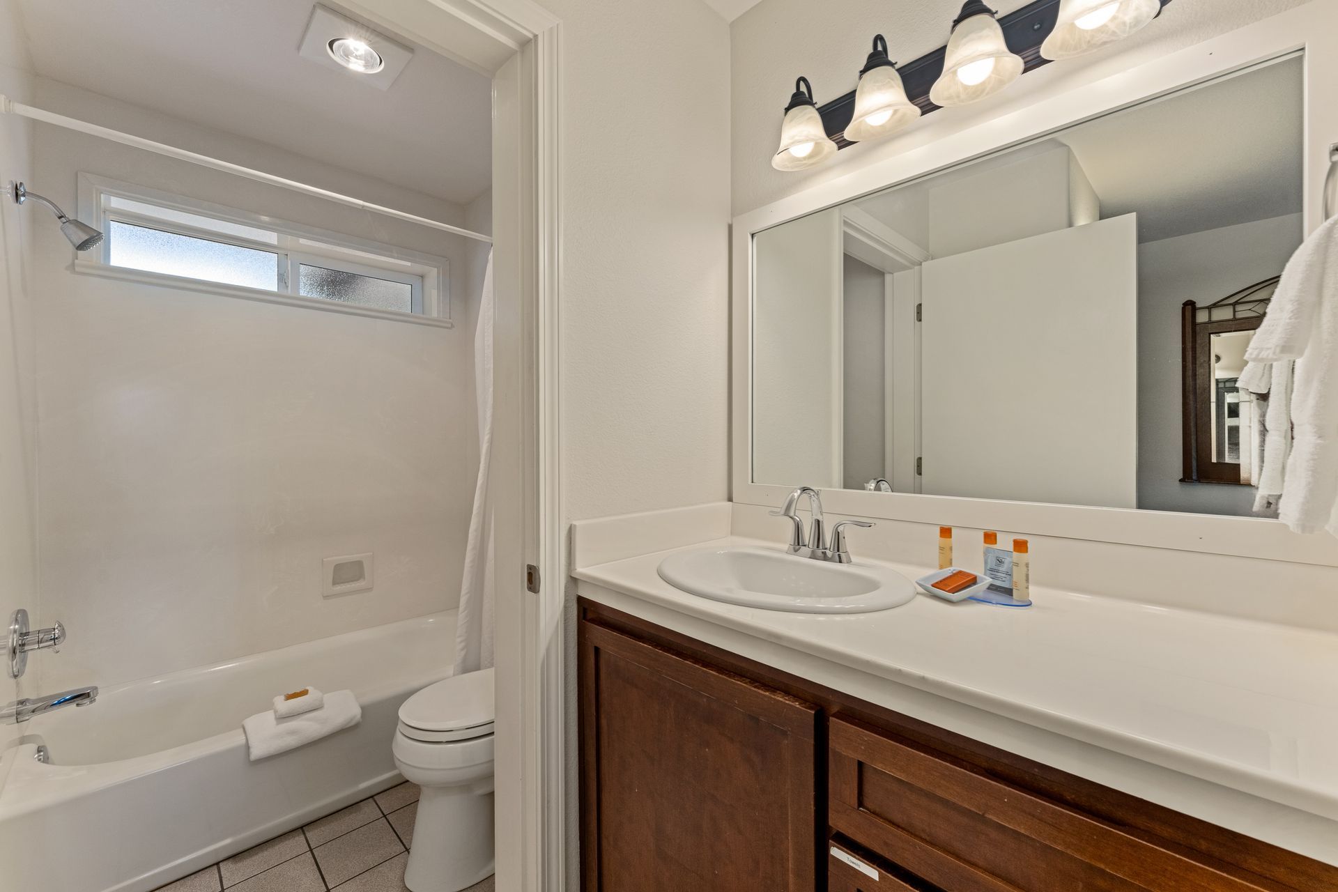 Small bathroom with tub and toilet on left and vanity with mirror and lights on right.