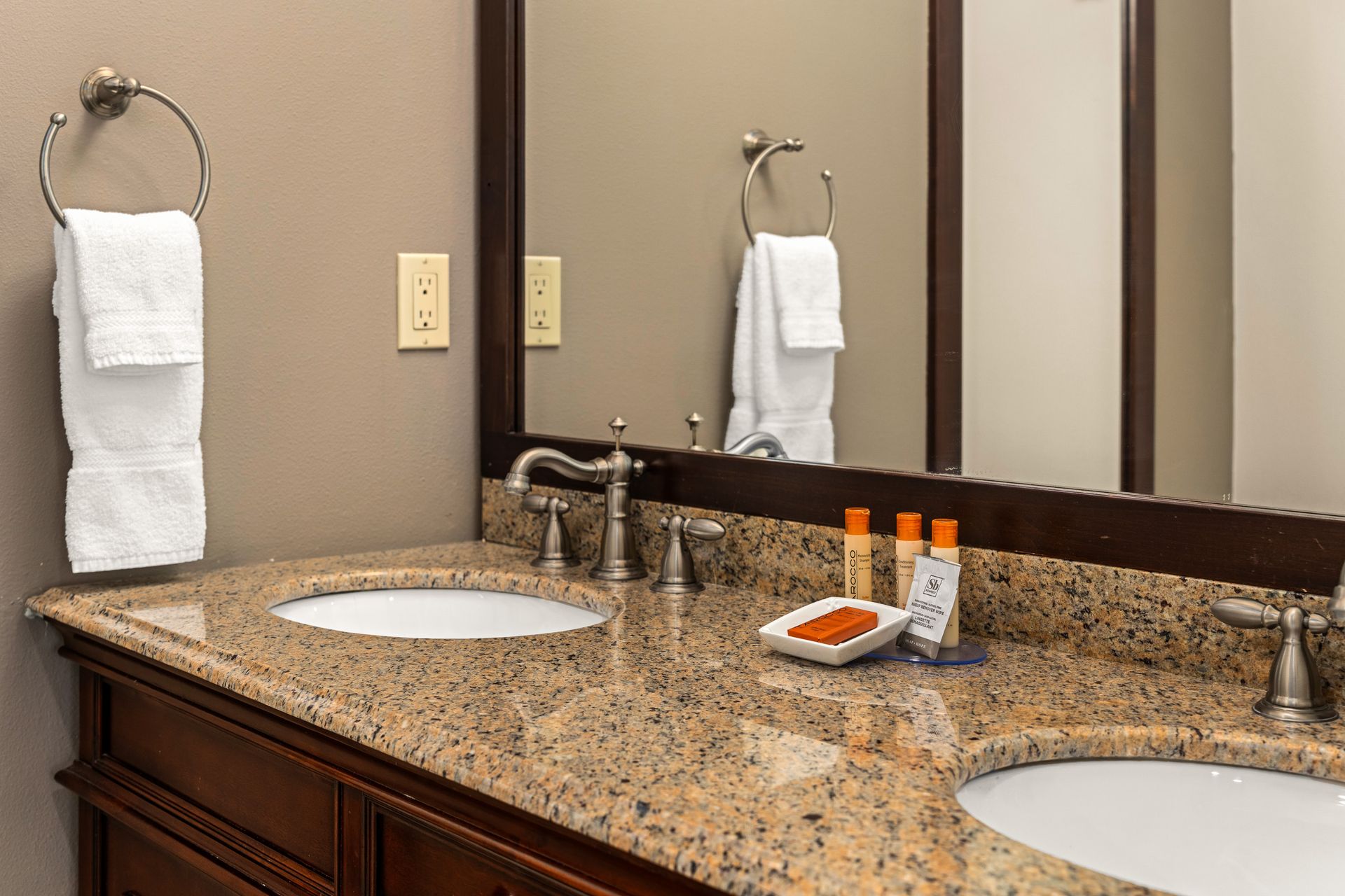 Bathroom vanity with granite countertop, two sinks, mirrors, and neatly folded white towels