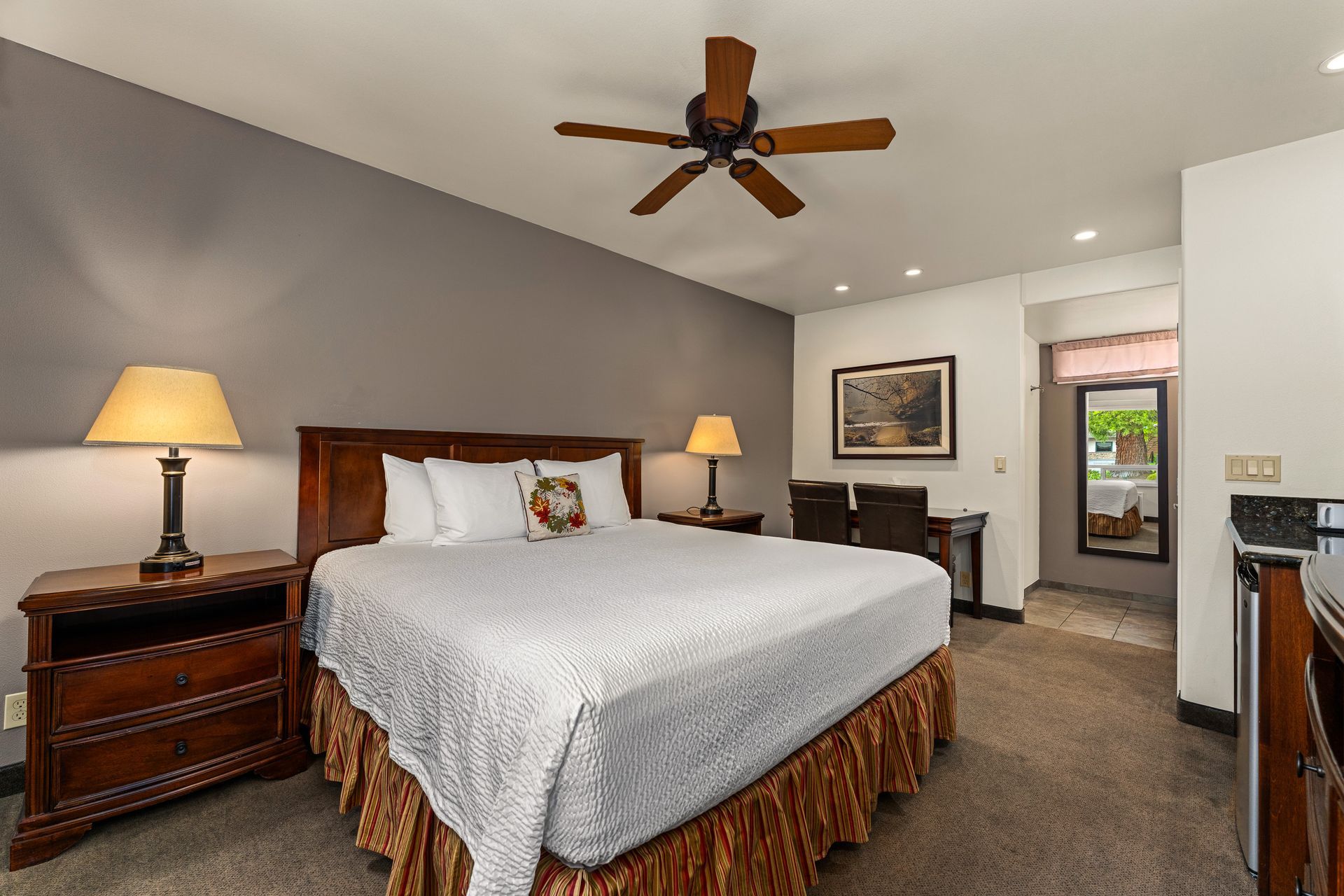 Spacious bedroom with a large bed, wood nightstands, ceiling fan, and carpeted floor.