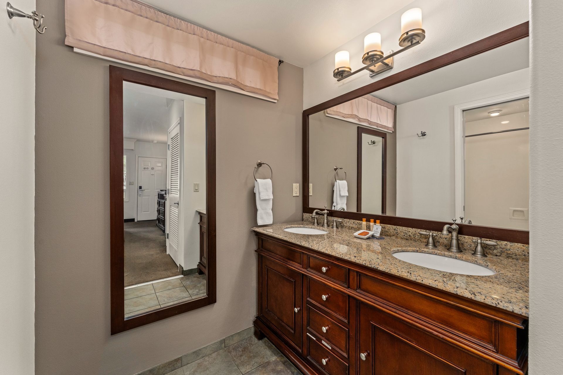 Modern bathroom vanity with double sinks, granite countertop, mirror, and wall sconces