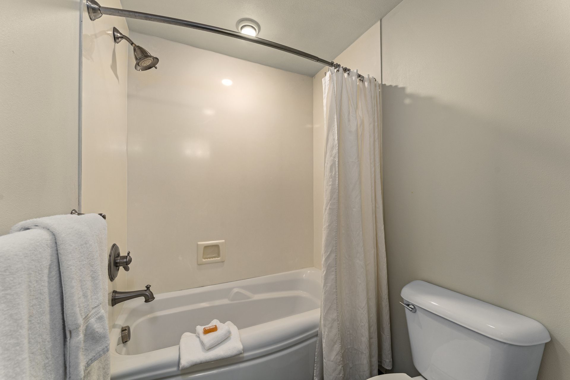 Small bathroom with a shower, white curtain, towel rack, and toilet visible.