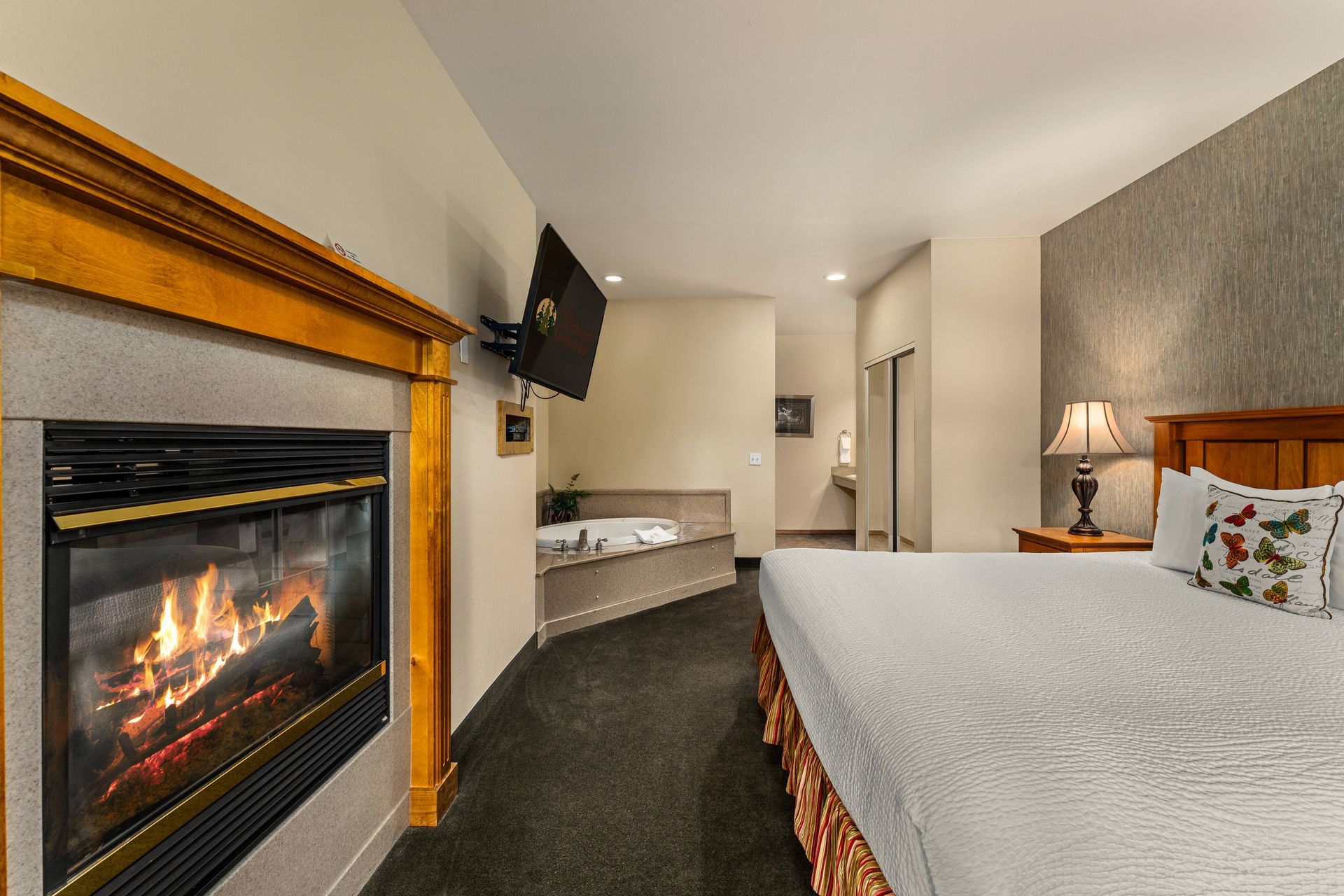 Bedroom with fireplace, wall-mounted TV, and two beds in a beige, carpeted hotel room