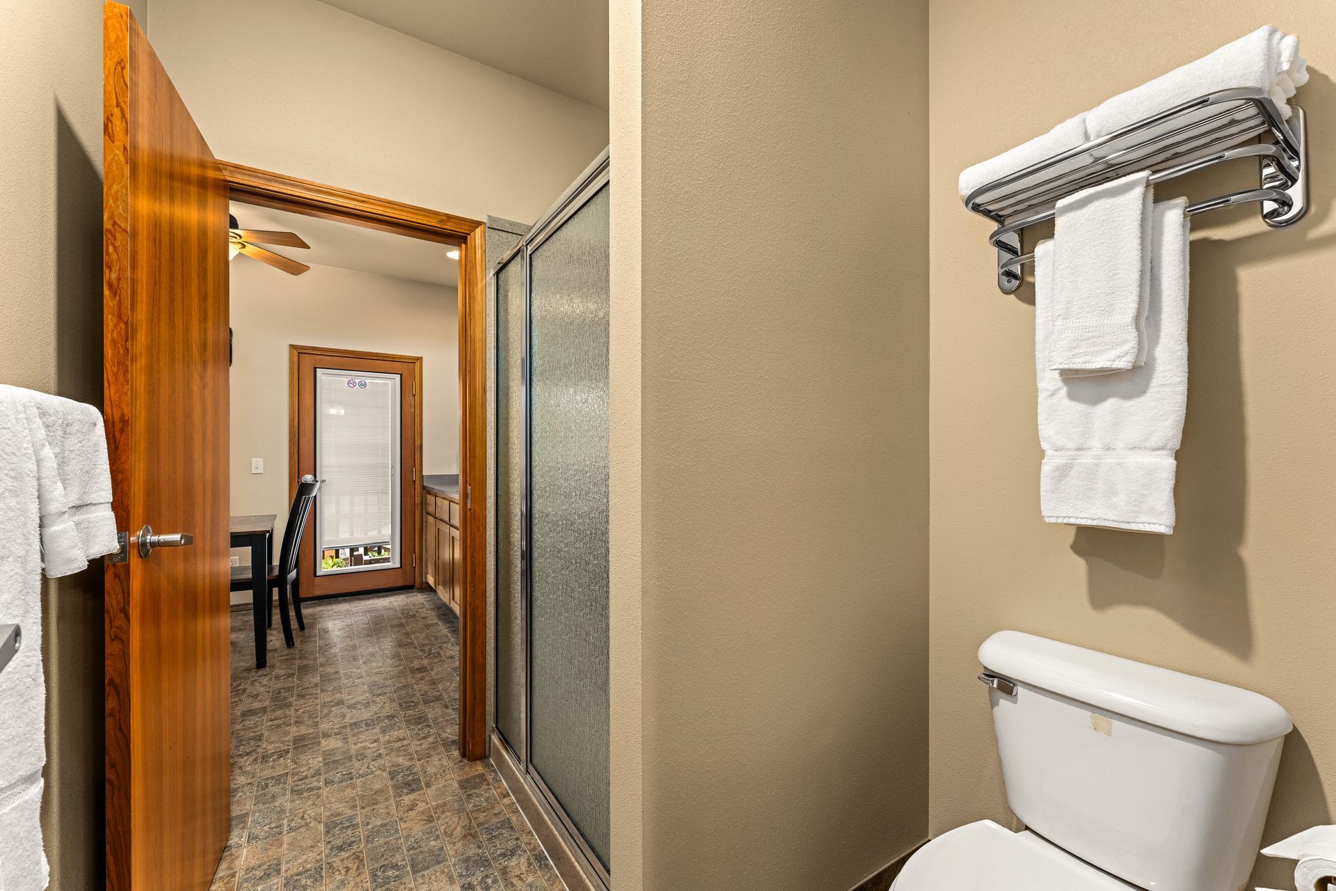 Narrow hotel hallway with open wooden doors and a bathroom towel rack and toilet in the foreground