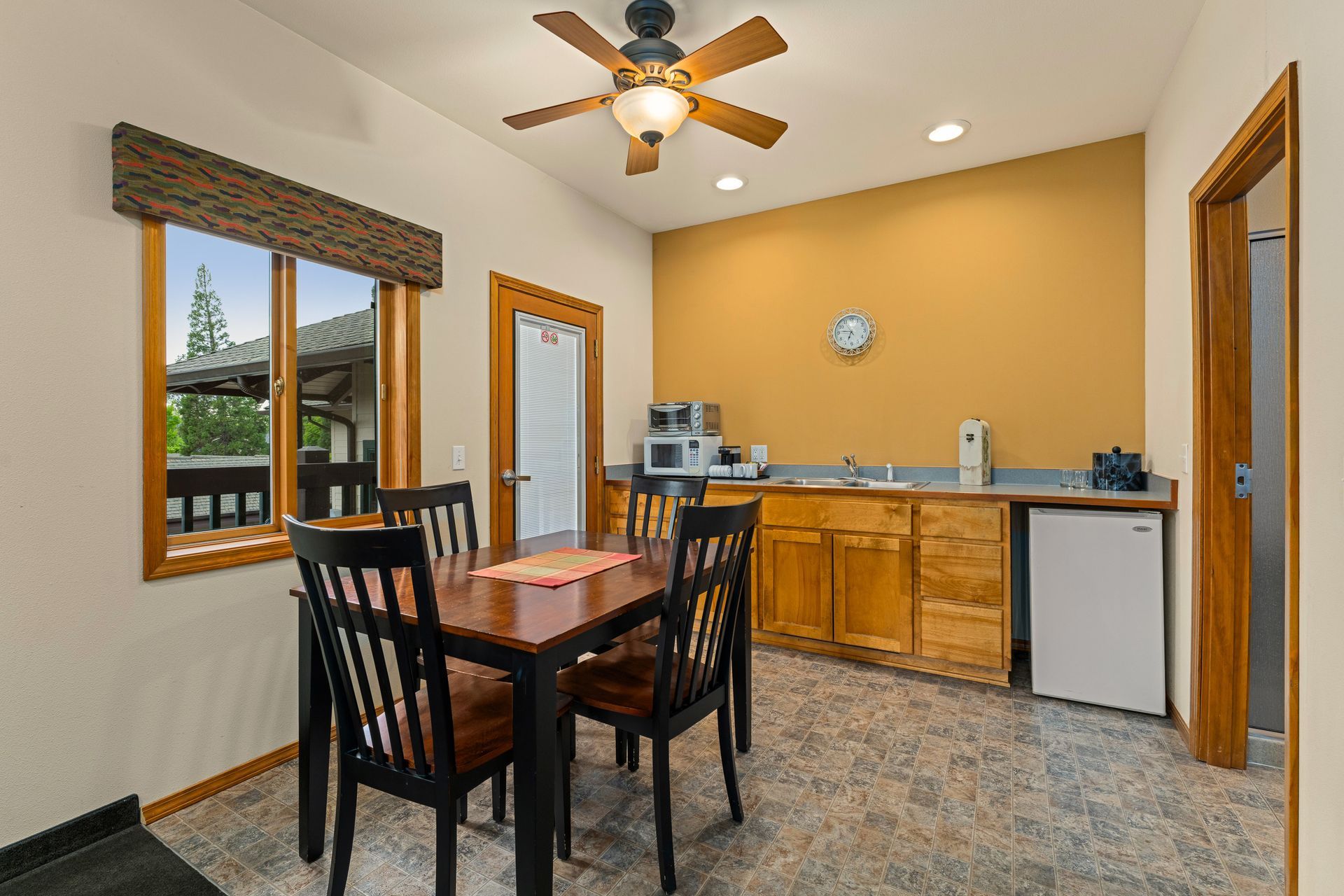 Dining area with wooden table and chairs, beige walls, ceiling fan, and kitchenette with cabinets and sink.