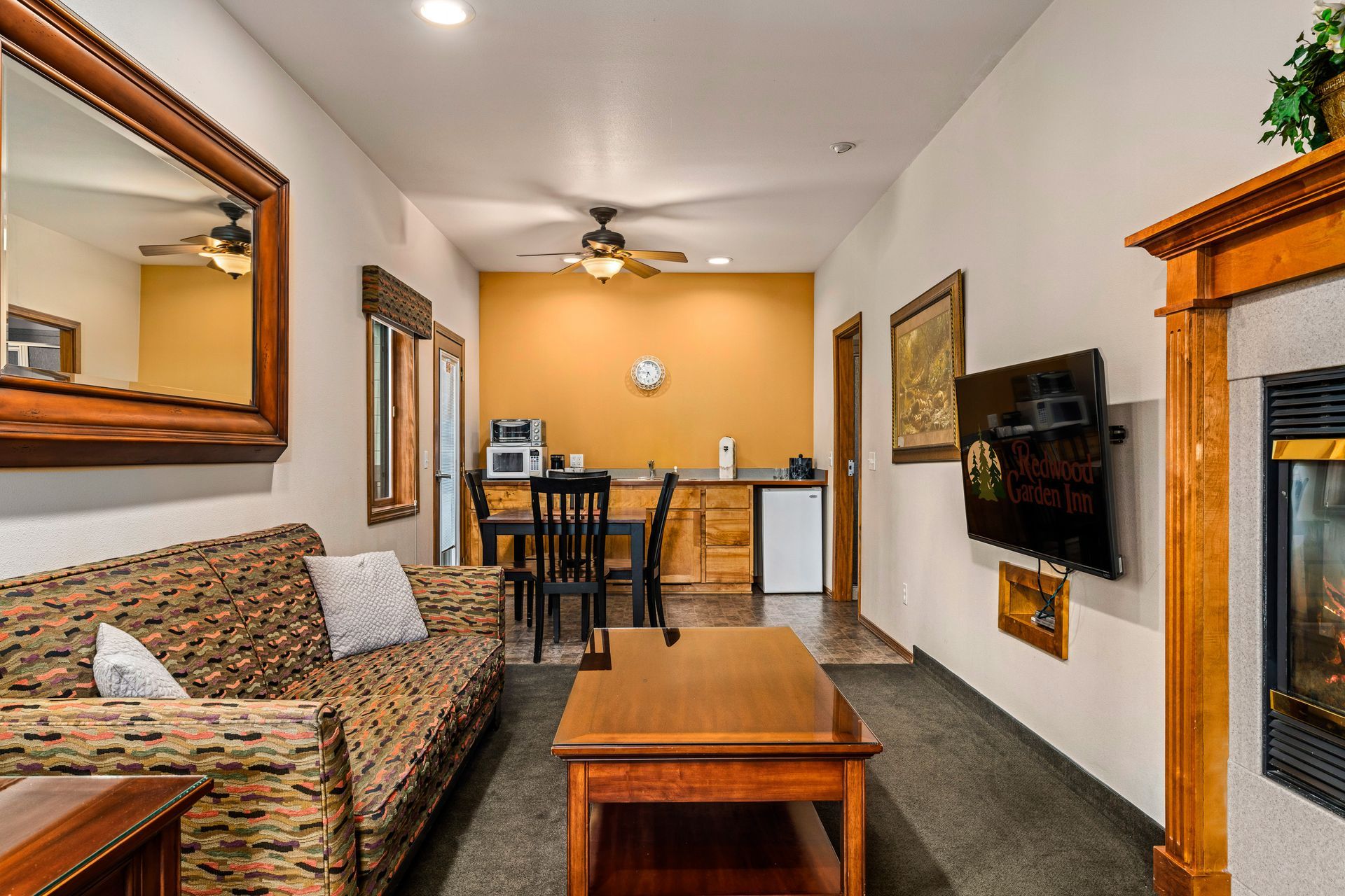 Cozy living room with patterned sofa, coffee table, wall-mounted TV, and open view to dining area and kitchen