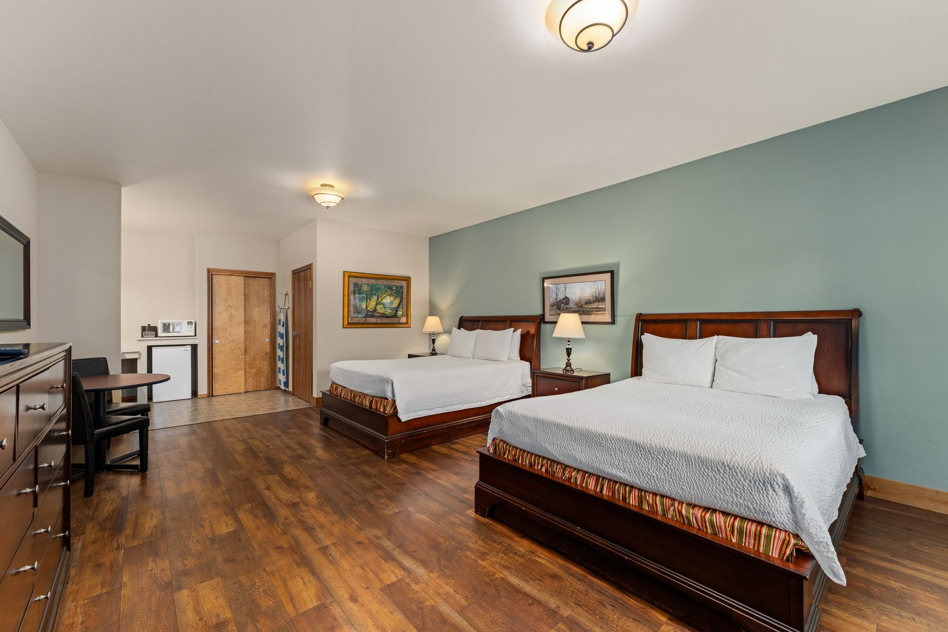 Spacious hotel room with two queen beds, hardwood floors, desk, and wall art