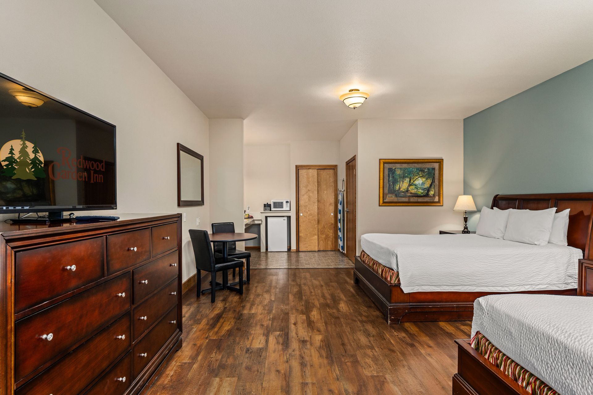 Bright bedroom with two beds, wood dresser, desk, and hardwood floor