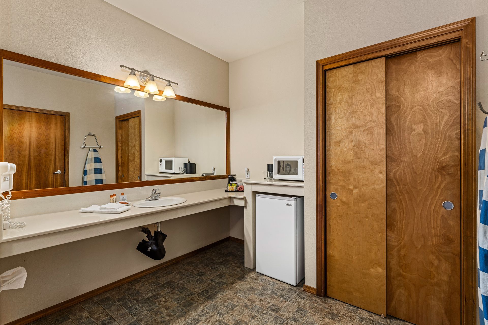 Public restroom vanity with large mirror, beige countertop, white sink, and wooden doors.