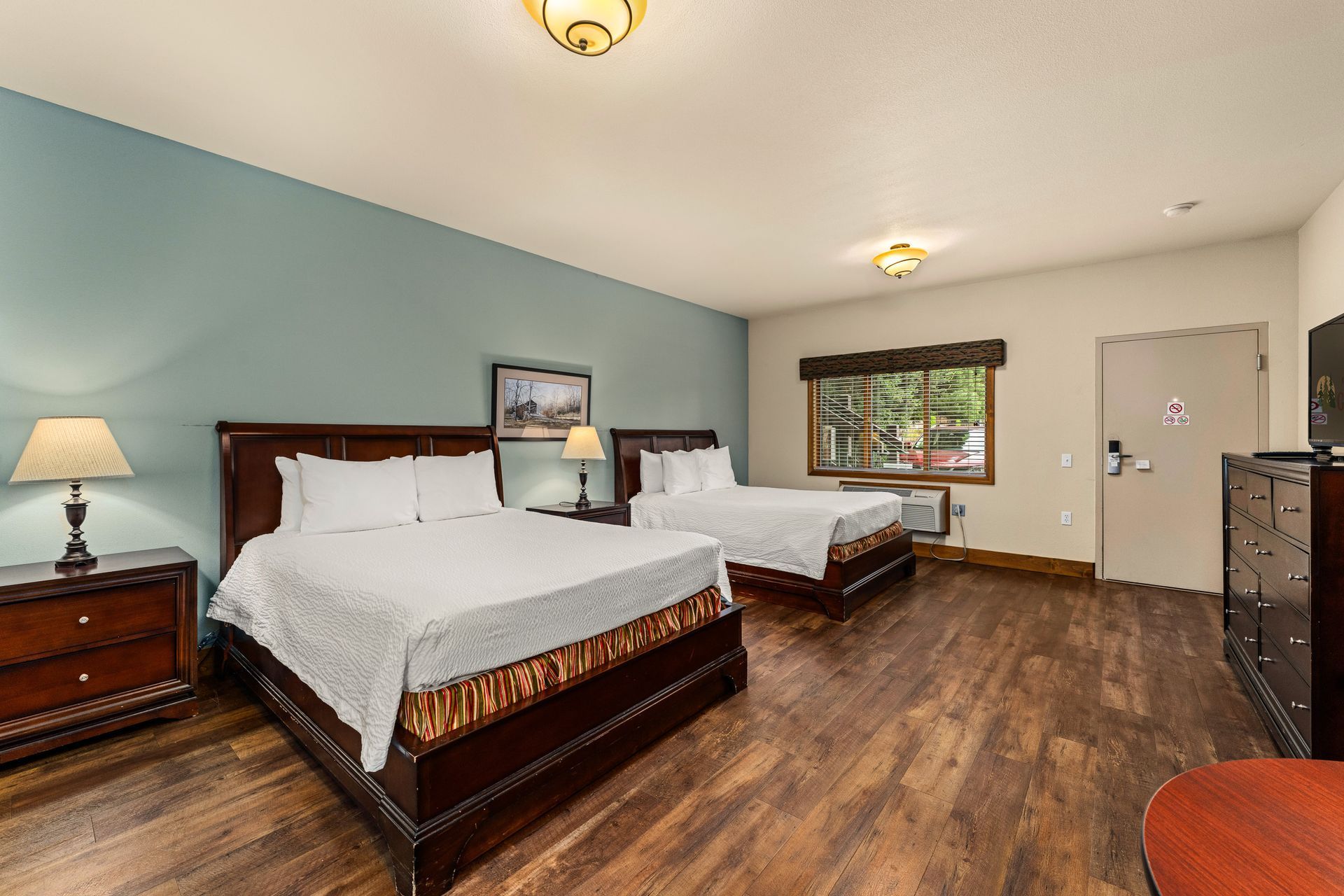 Bright bedroom with two beds, wood furniture, a window, and blue walls