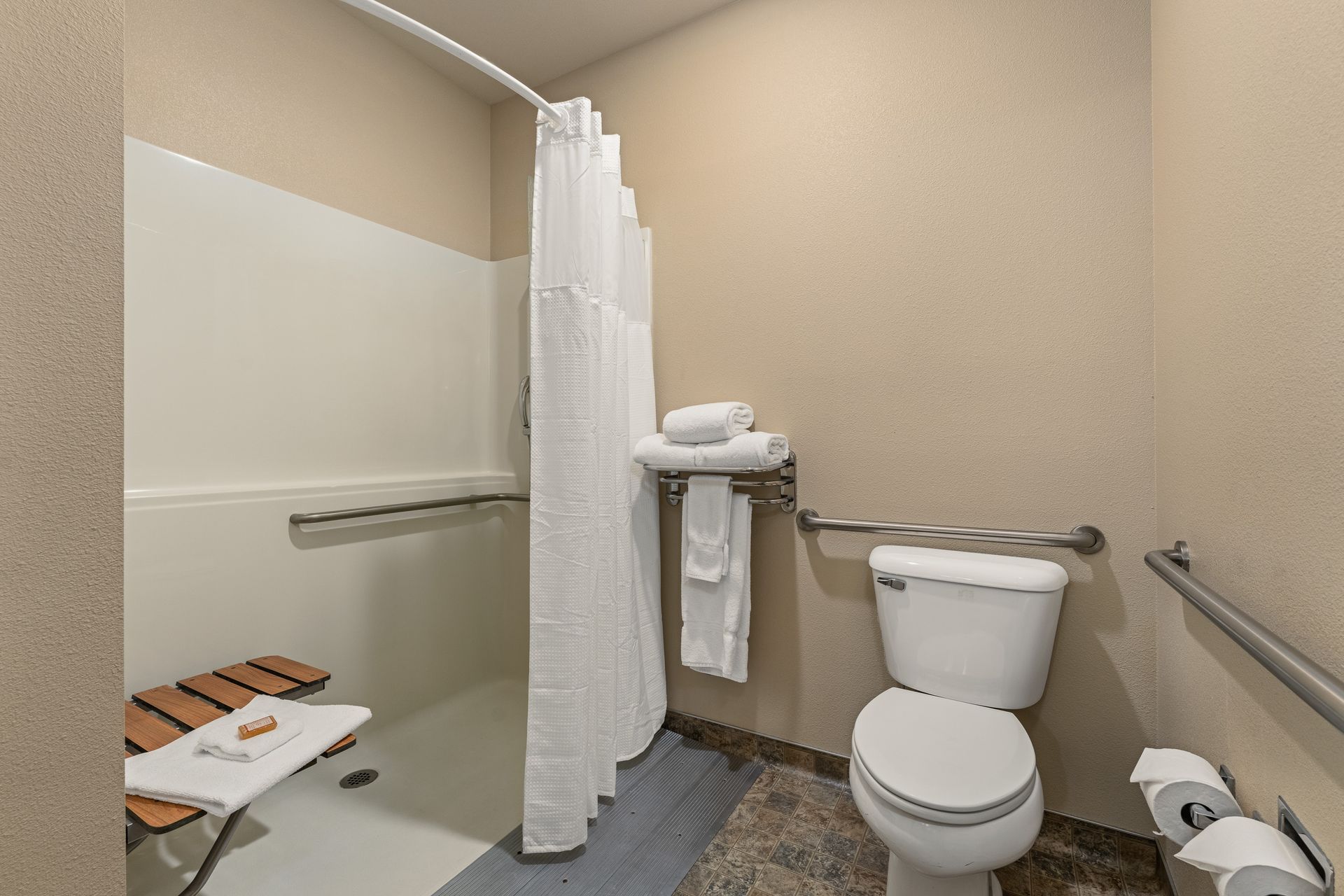 Accessible bathroom with toilet, shower chair, grab bars, and a shower curtain.