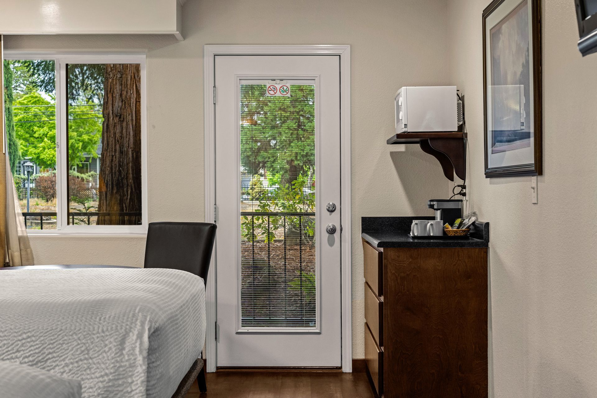 Bedroom interior with bed, balcony door, window, and a small cabinet with coffee maker