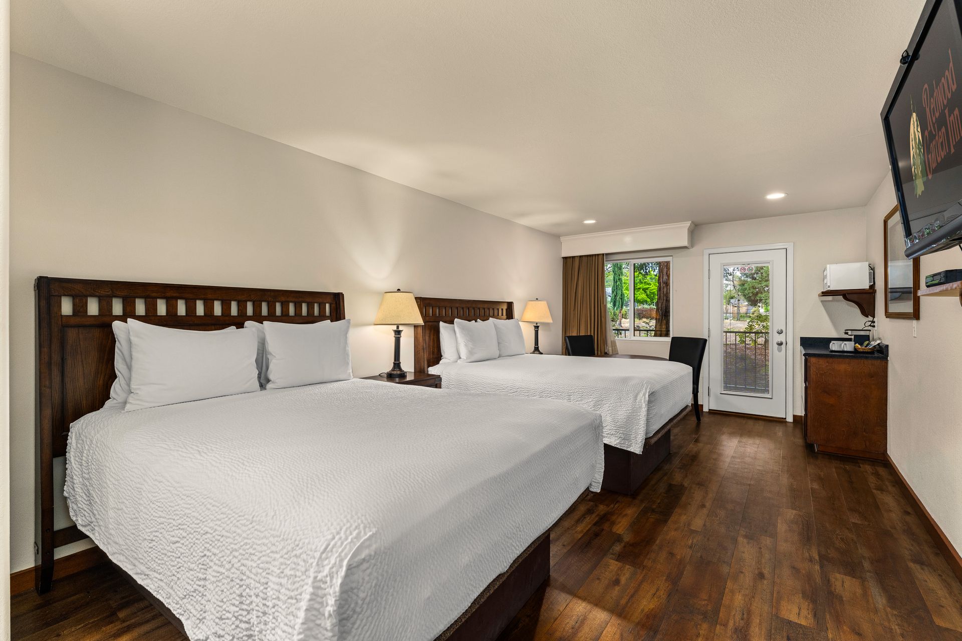 Hotel room with two double beds, wood floors, and a TV on the wall