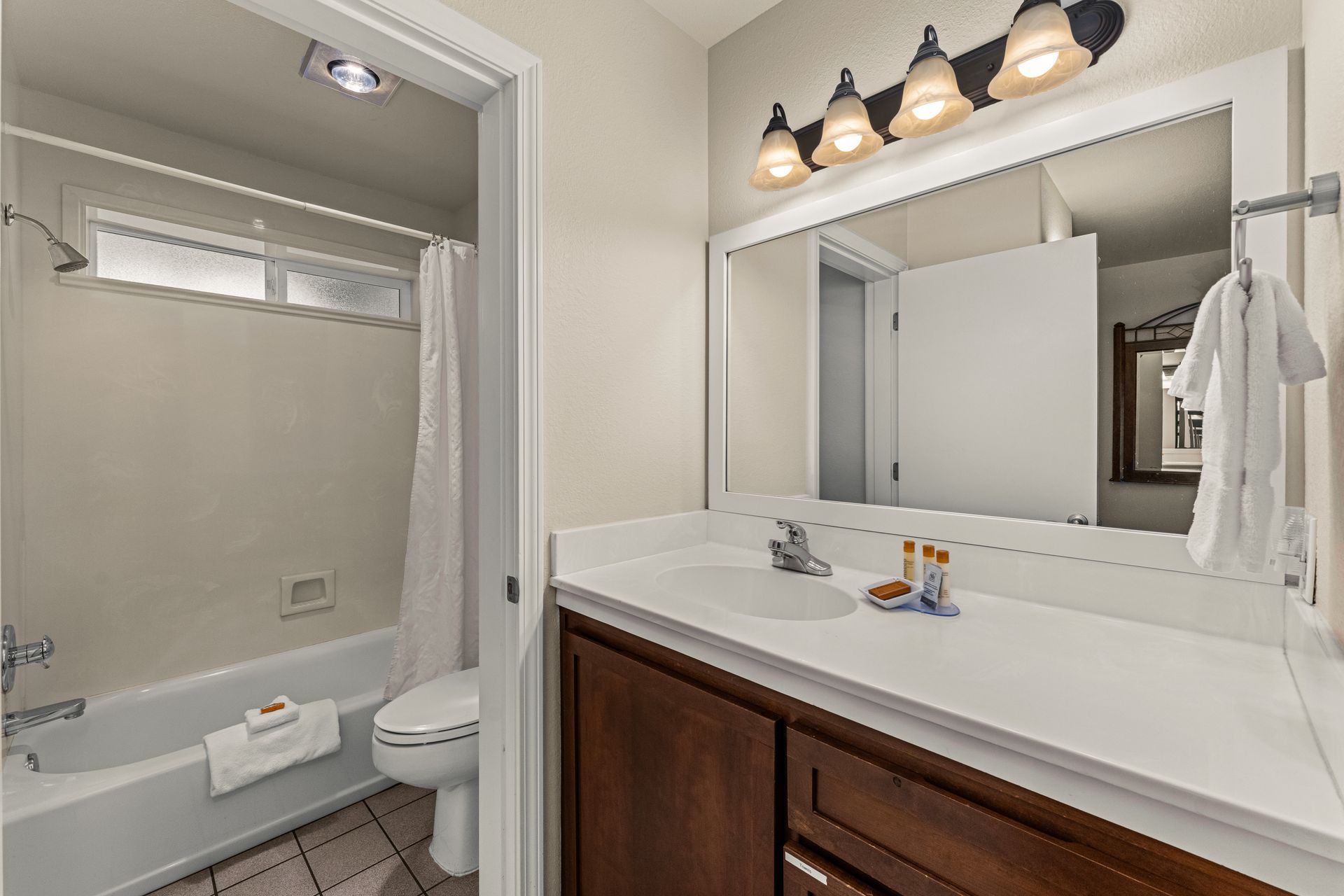 Bathroom vanity and shower area with white countertop, dark wood cabinet, and mirror lights.
