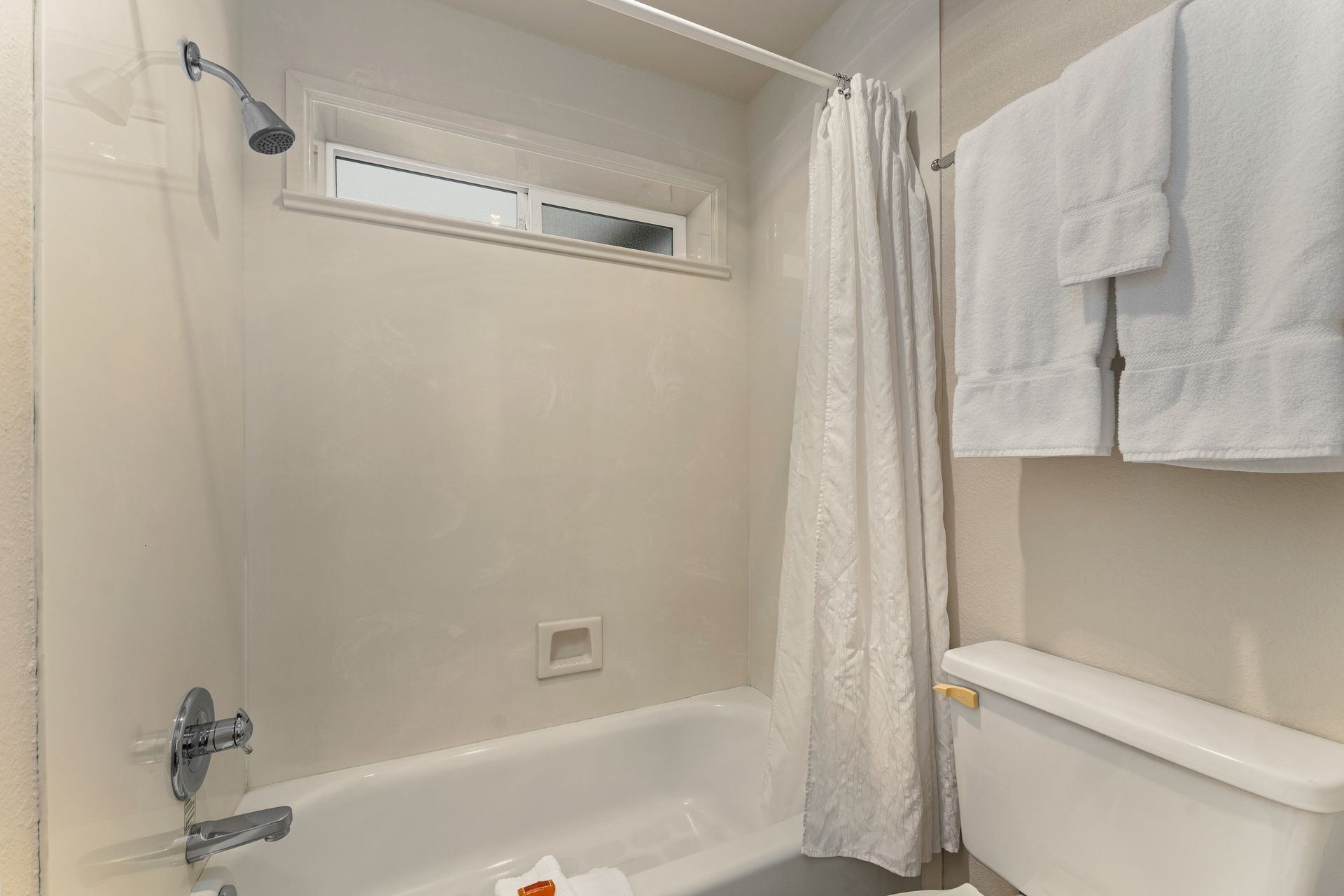 Small white bathroom with bathtub, shower curtain, towel rack, and toilet seat visible