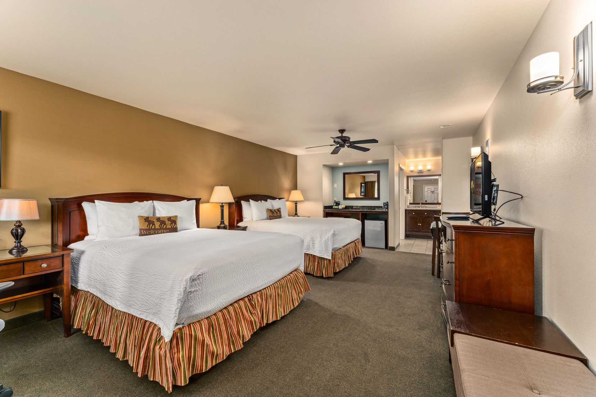 Hotel room with two beds, lamps, dresser, and TV in a long carpeted suite