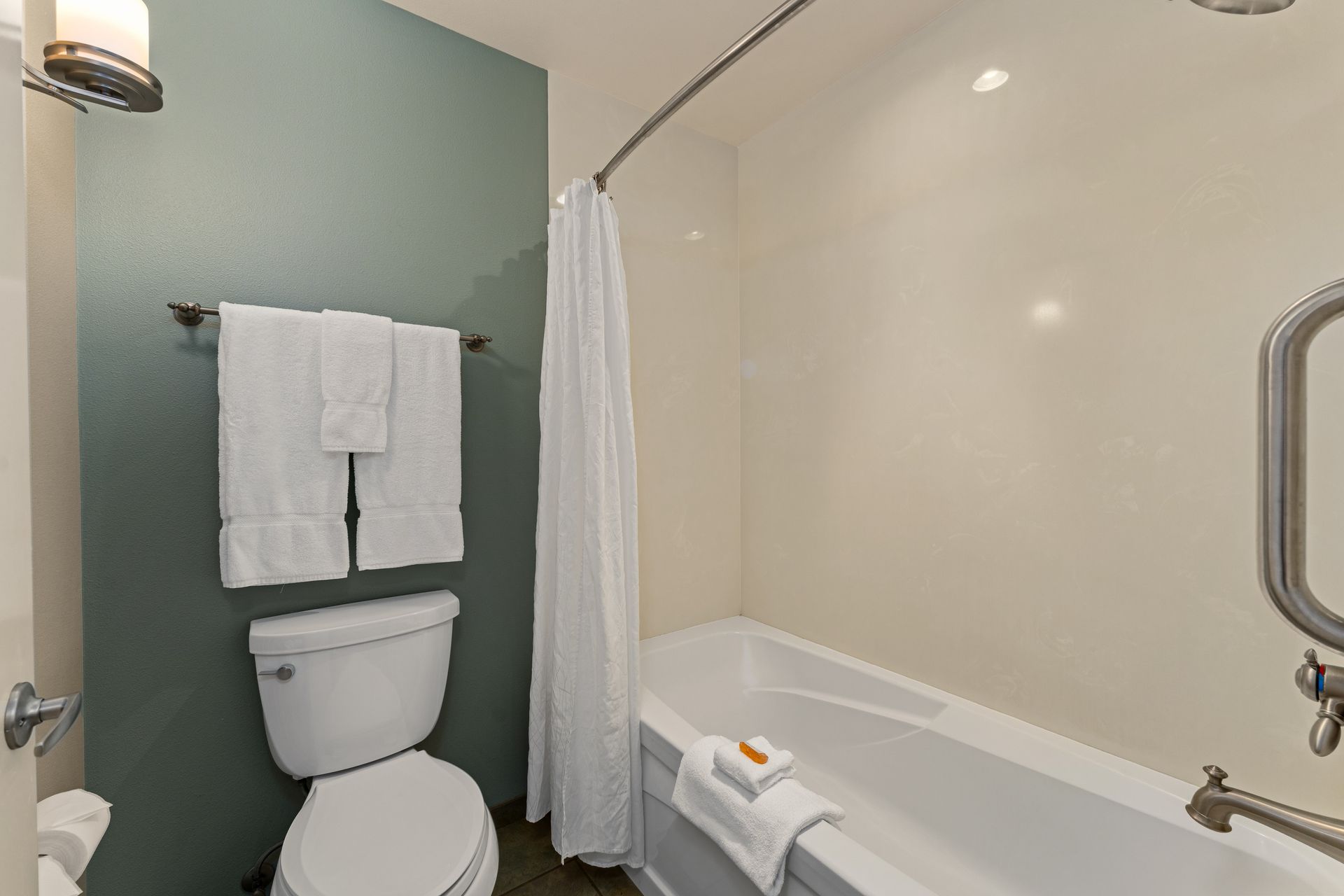 Compact bathroom with toilet, towel rack, and shower-tub with white curtain and grab bar