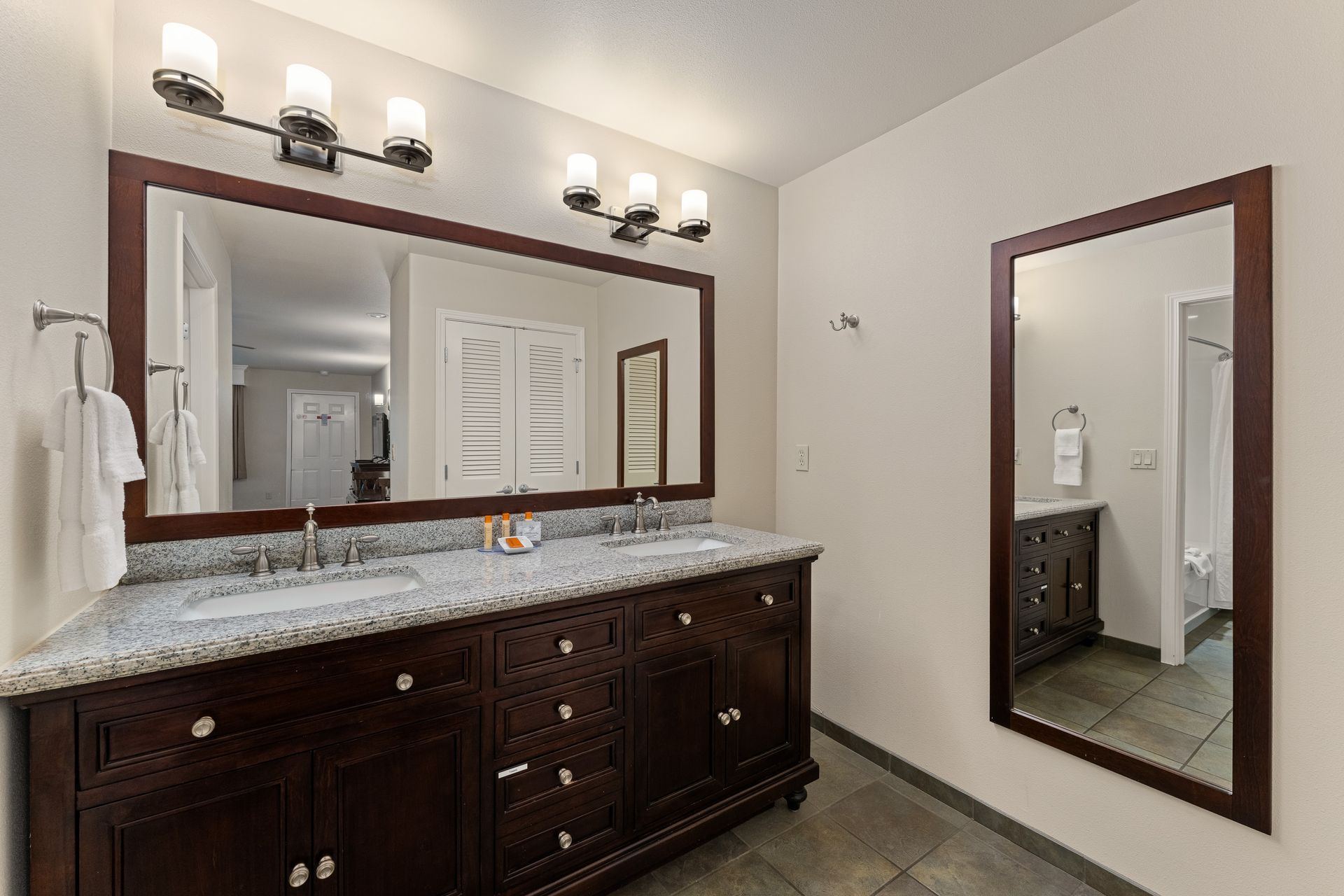 Bathroom vanity with granite countertop, large mirror, and wall sconces in a bright, tiled room