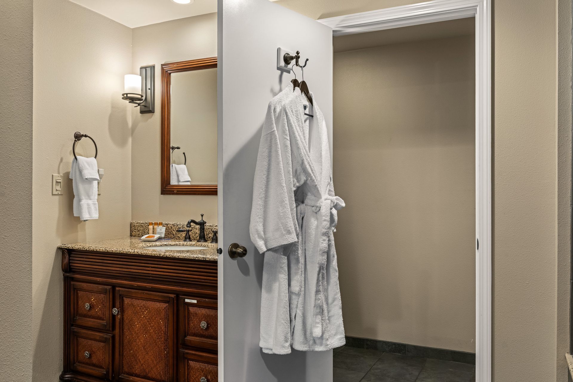 Bathroom vanity with mirror beside an open closet door holding two white robes.