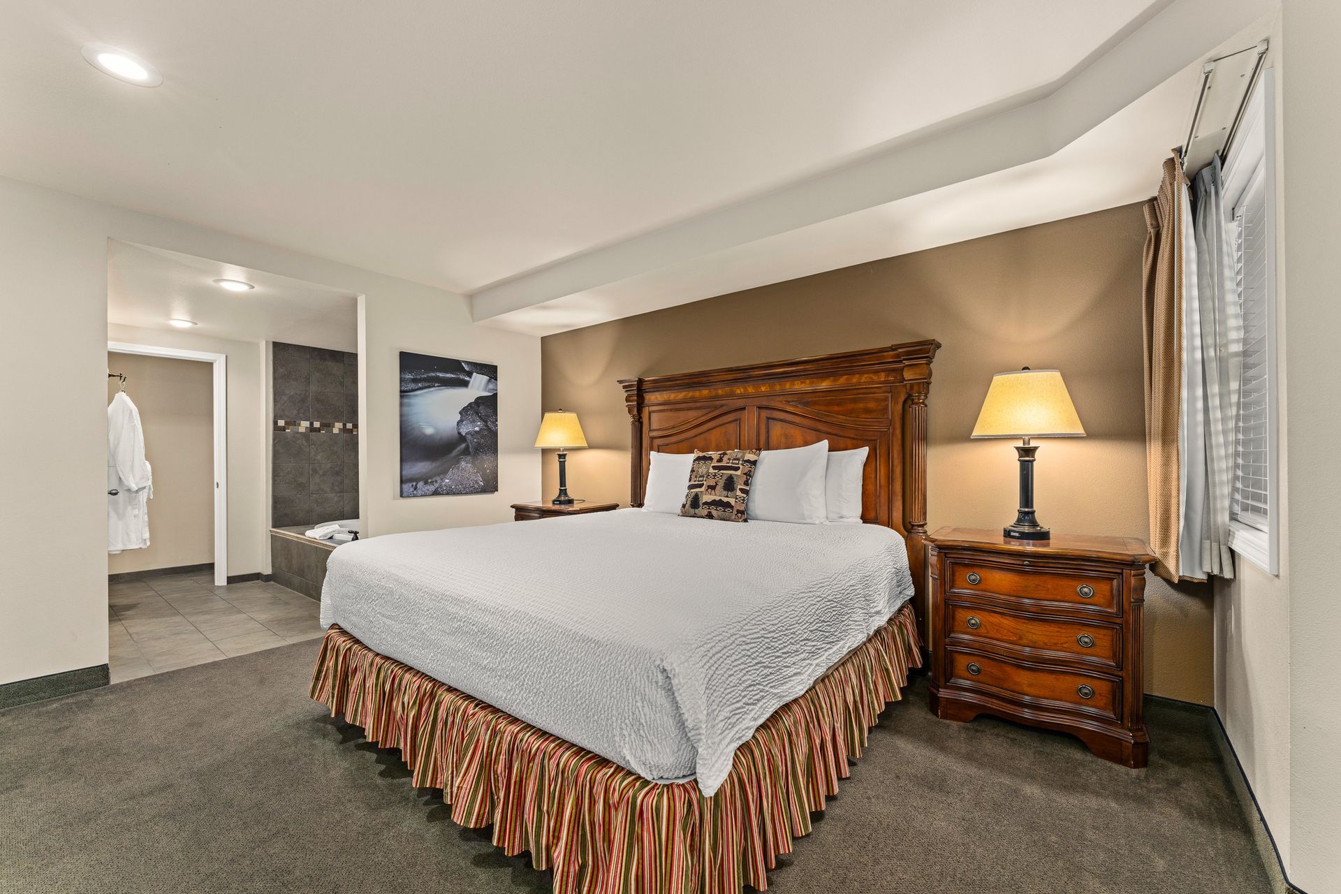Spacious hotel bedroom with a large bed, wooden headboard, bedside lamps, and beige walls