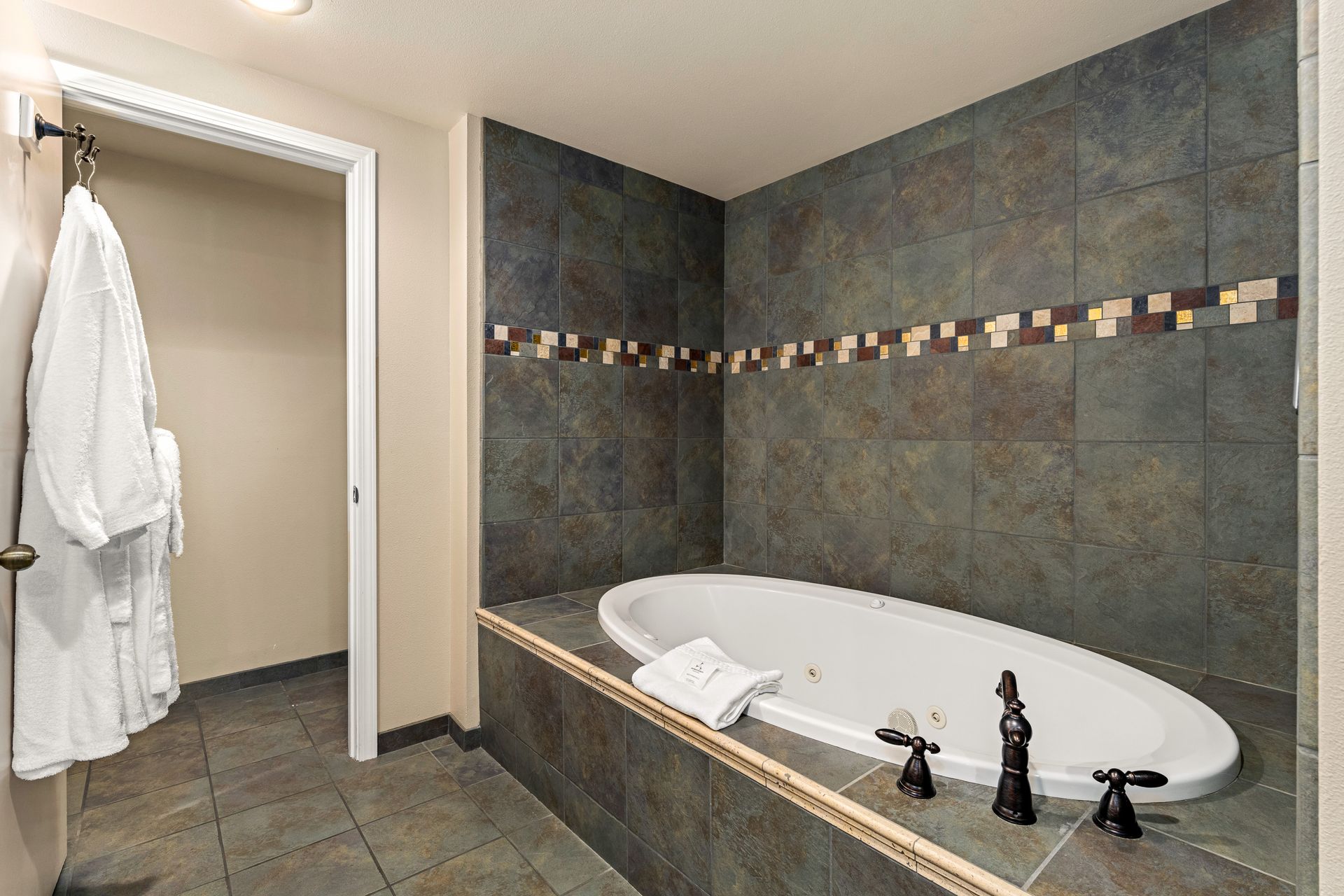 Bathroom with a tiled soaking tub, dark walls, and an open doorway with a hanging robe