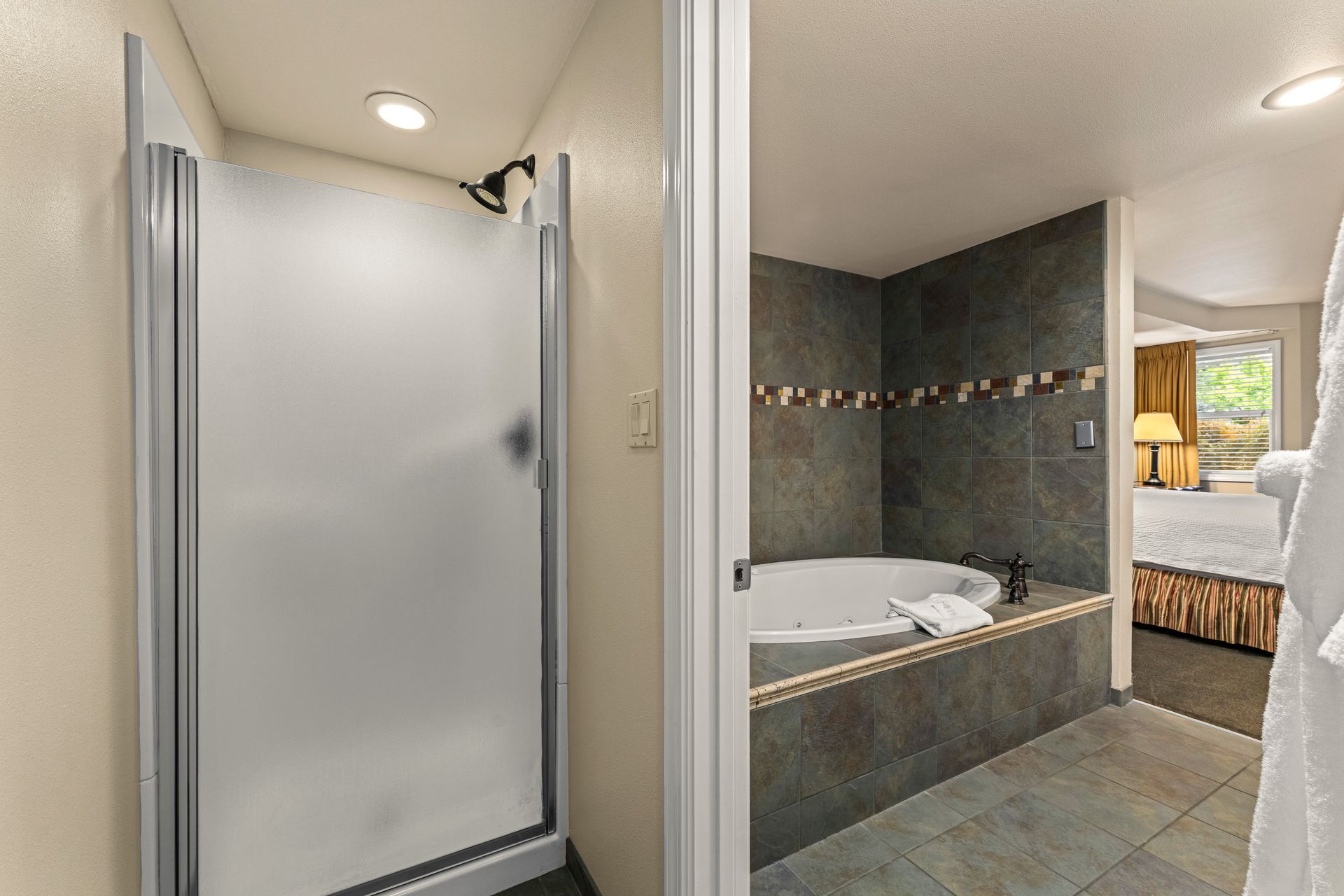 Bathroom with frosted glass shower, corner tub, and tiled walls leading to a bedroom view