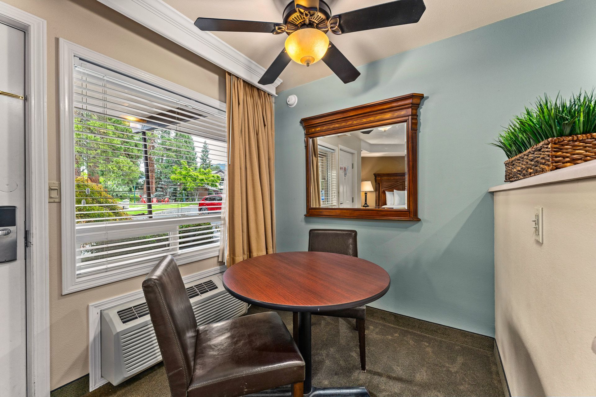 Small dining nook with round table, two chairs, window blinds, mirror, and ceiling fan in a blue room