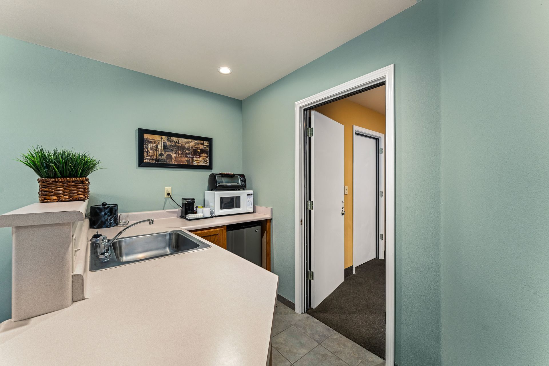Empty office reception area with teal walls, white counter, desk, and open doorway to a hallway
