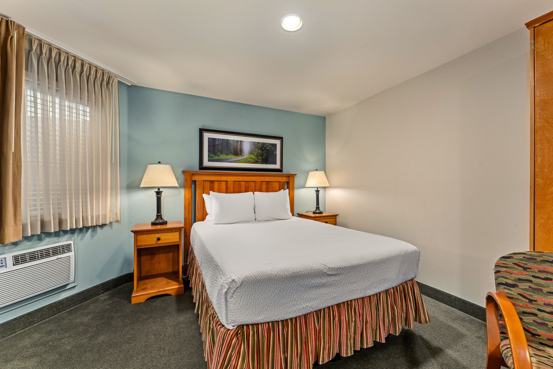 Cozy bedroom with a queen bed, nightstands, lamps, window curtains, and framed wall art