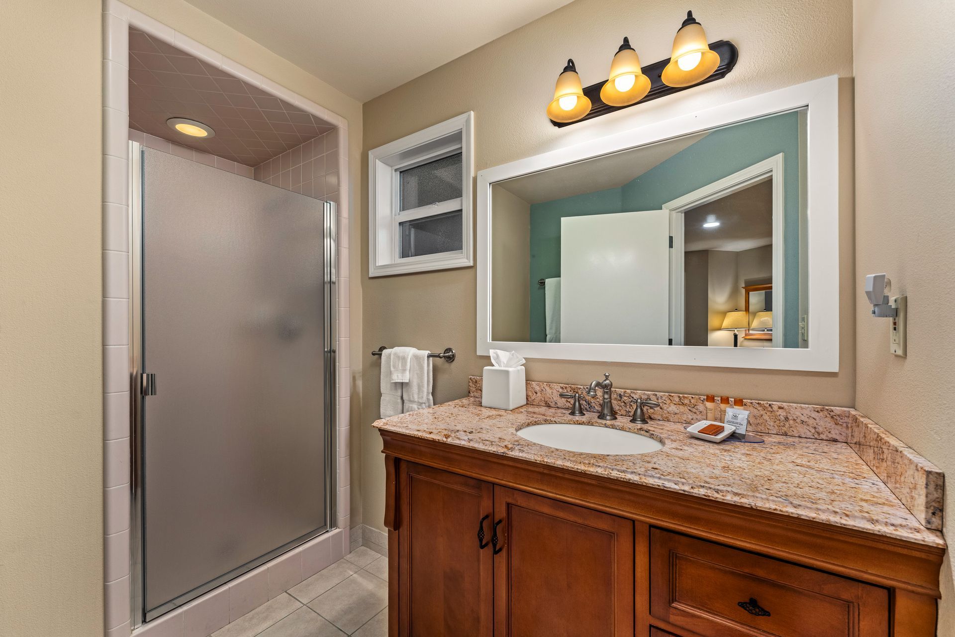 Bathroom with granite vanity, large mirror, three-light fixture, and glass shower stall
