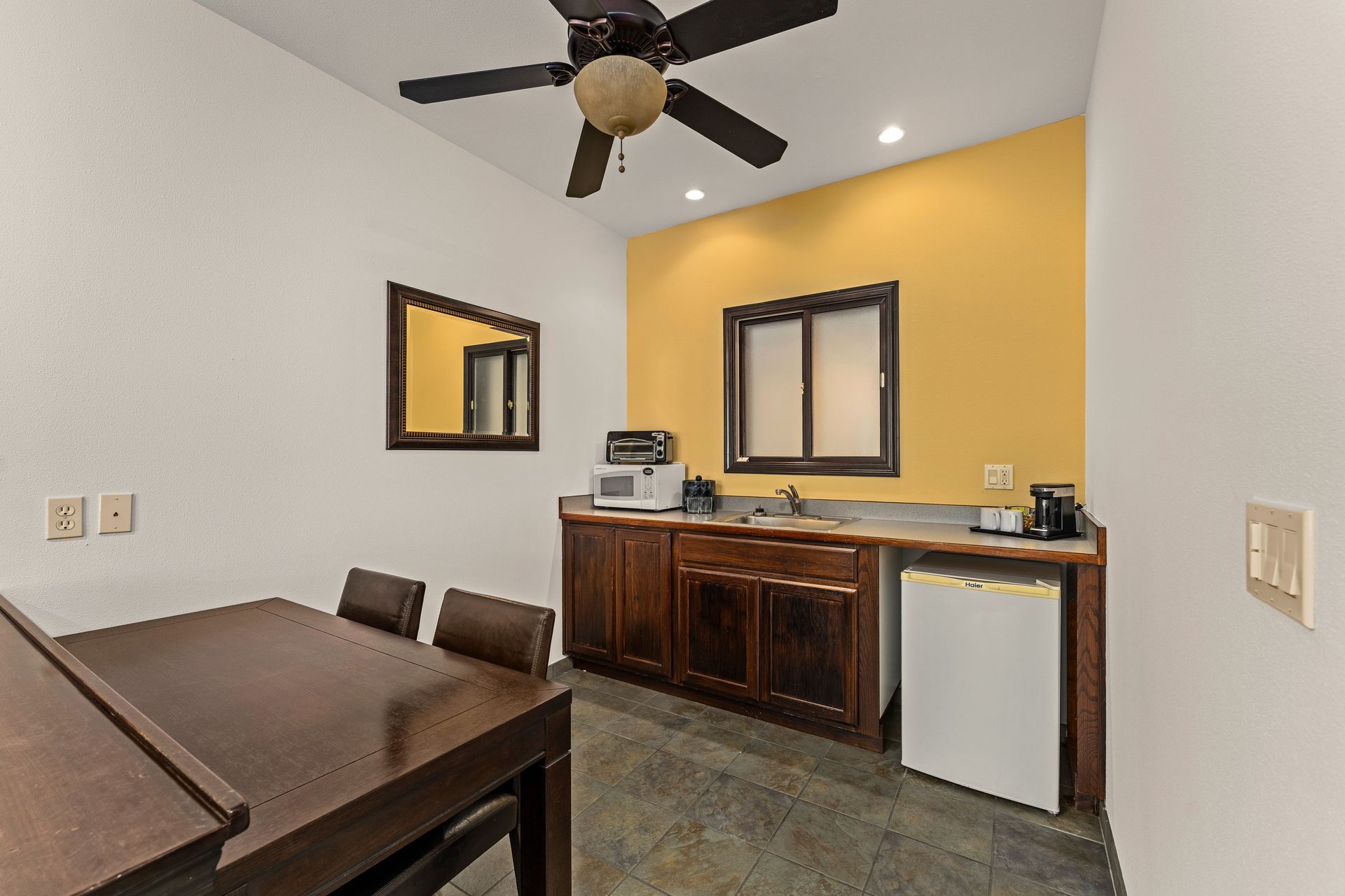 Bedroom with wood furniture, ceiling fan, and yellow accent wall with mirror and window.