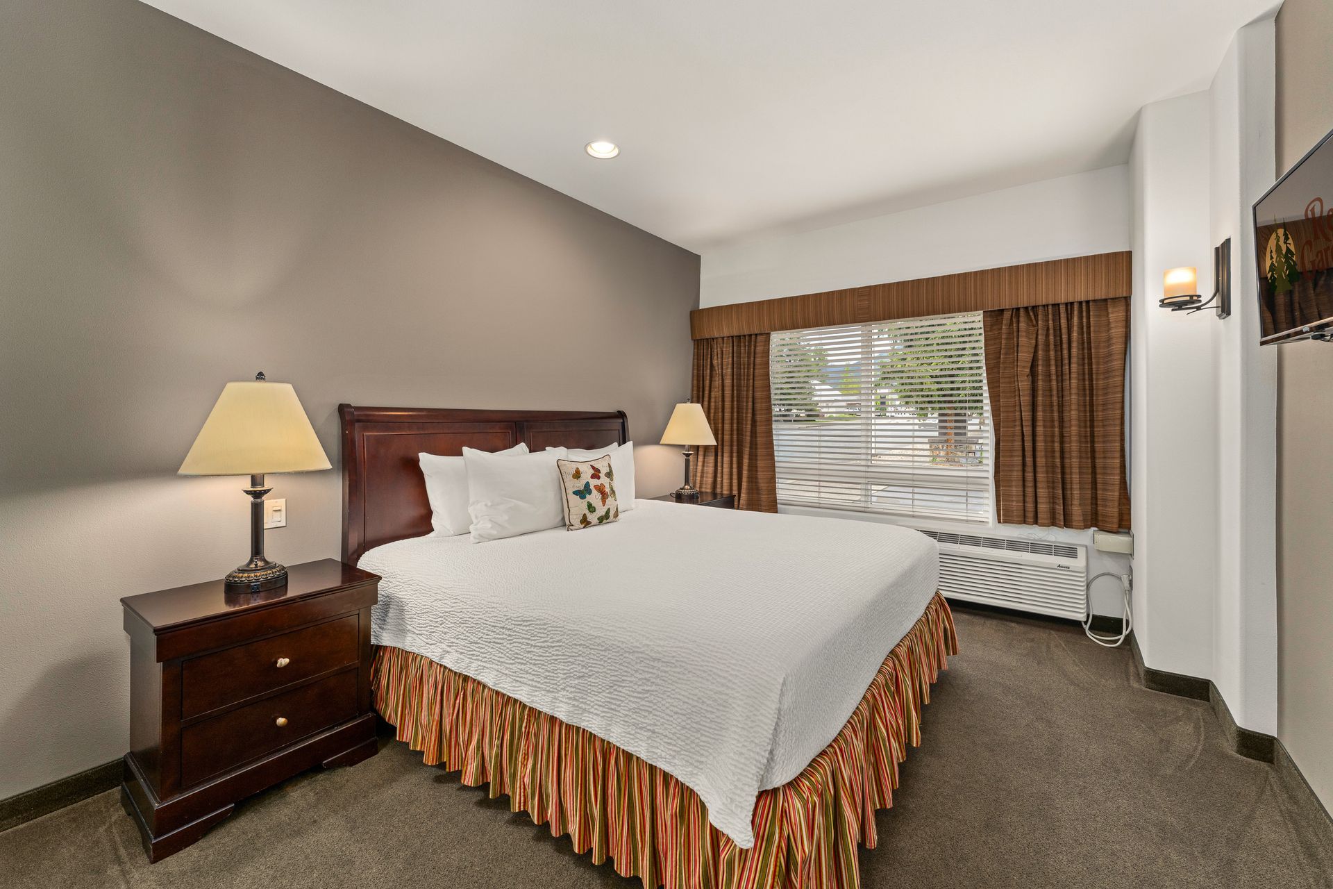 Hotel bedroom with a king bed, two lamps, and a large window with curtains