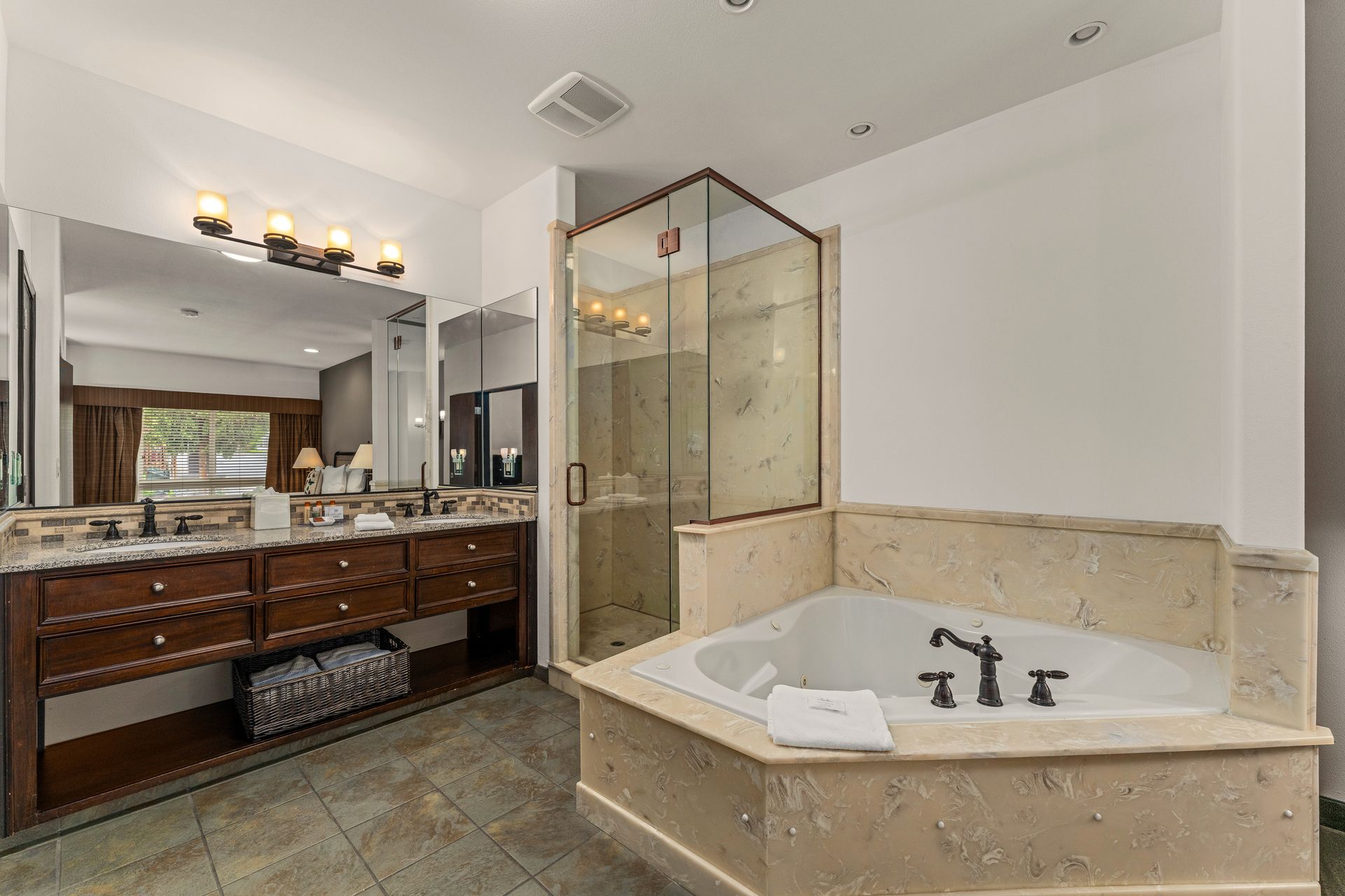 Spacious bathroom with double vanity, glass shower, and corner soaking tub in beige stone