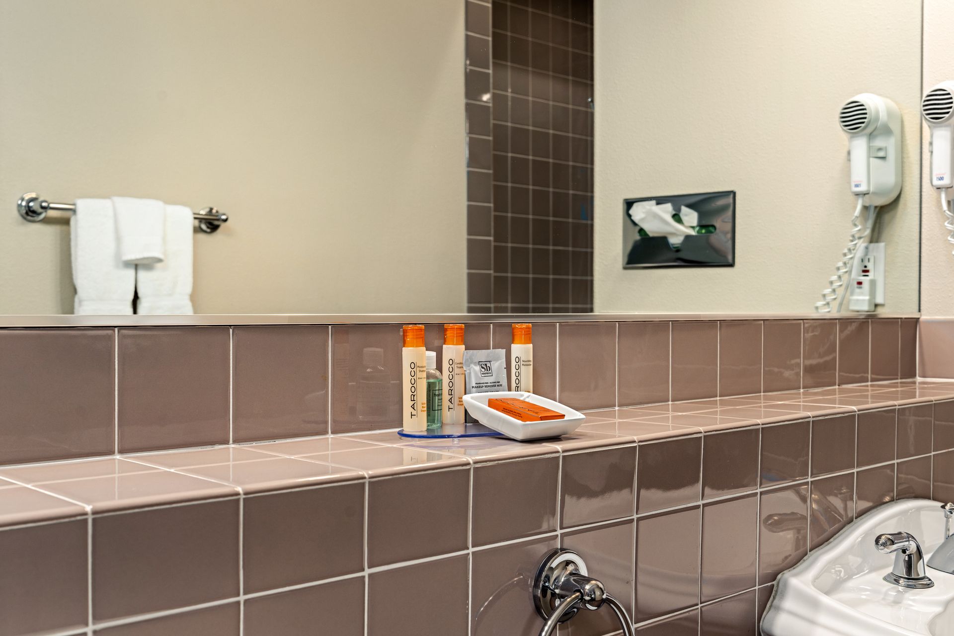 Public restroom countertop with hand soap bottles, paper towels, sink, and wall-mounted hair dryer.