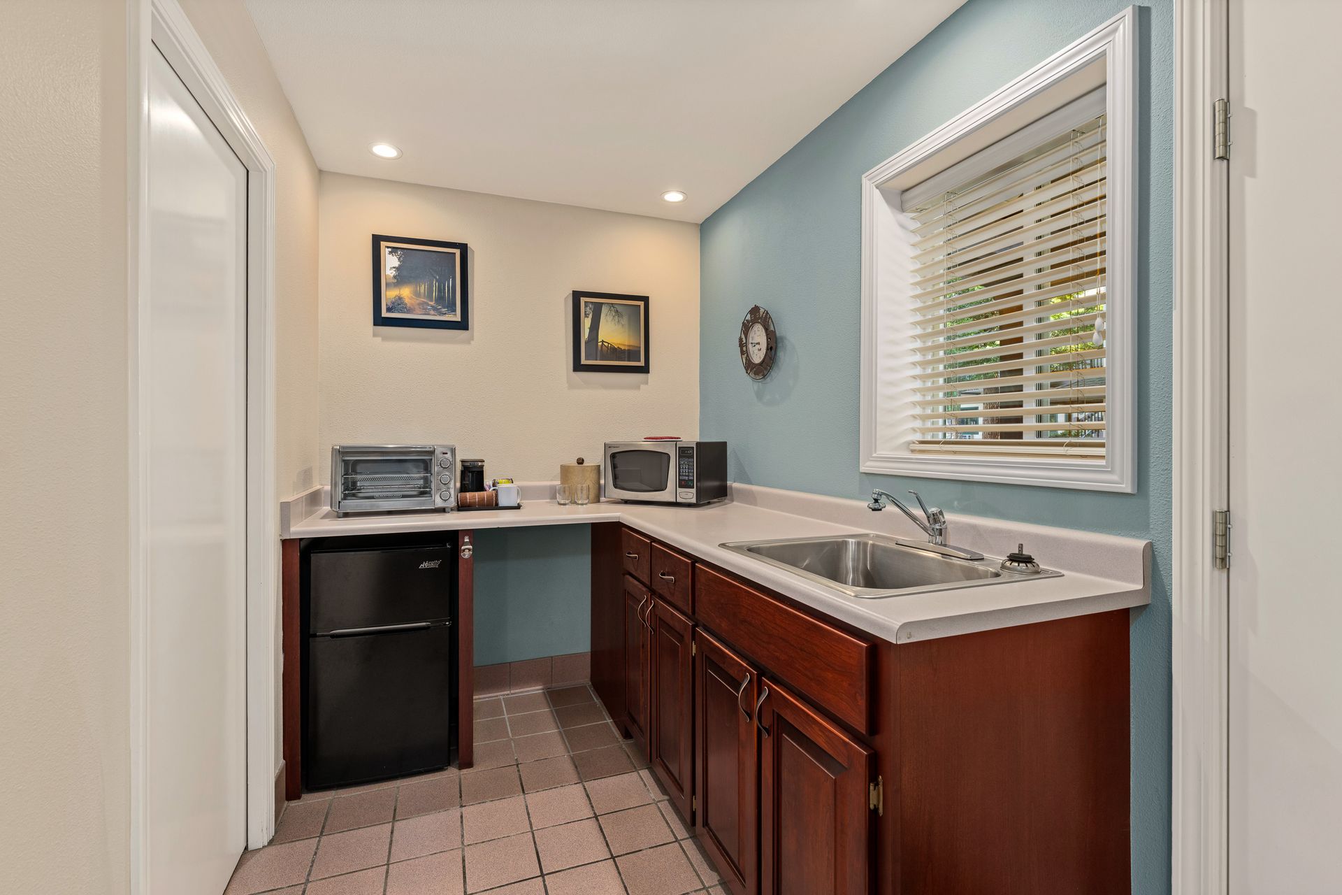 Bright laundry room with sink, folding counter, cabinets, and window blinds on blue walls