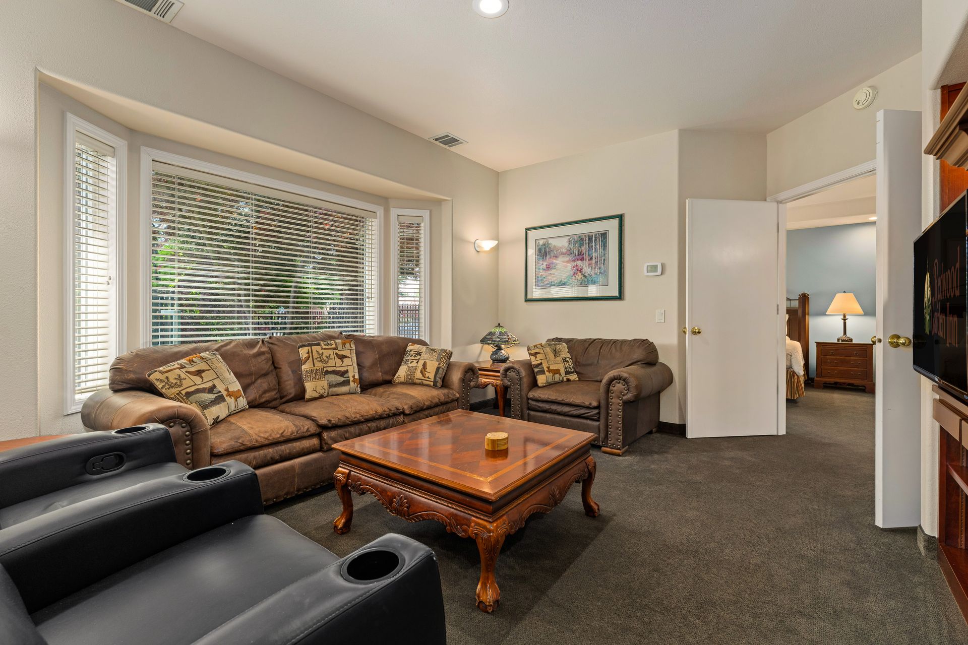 Living room with brown sofas, black armchair, wooden coffee table, and bay window with blinds