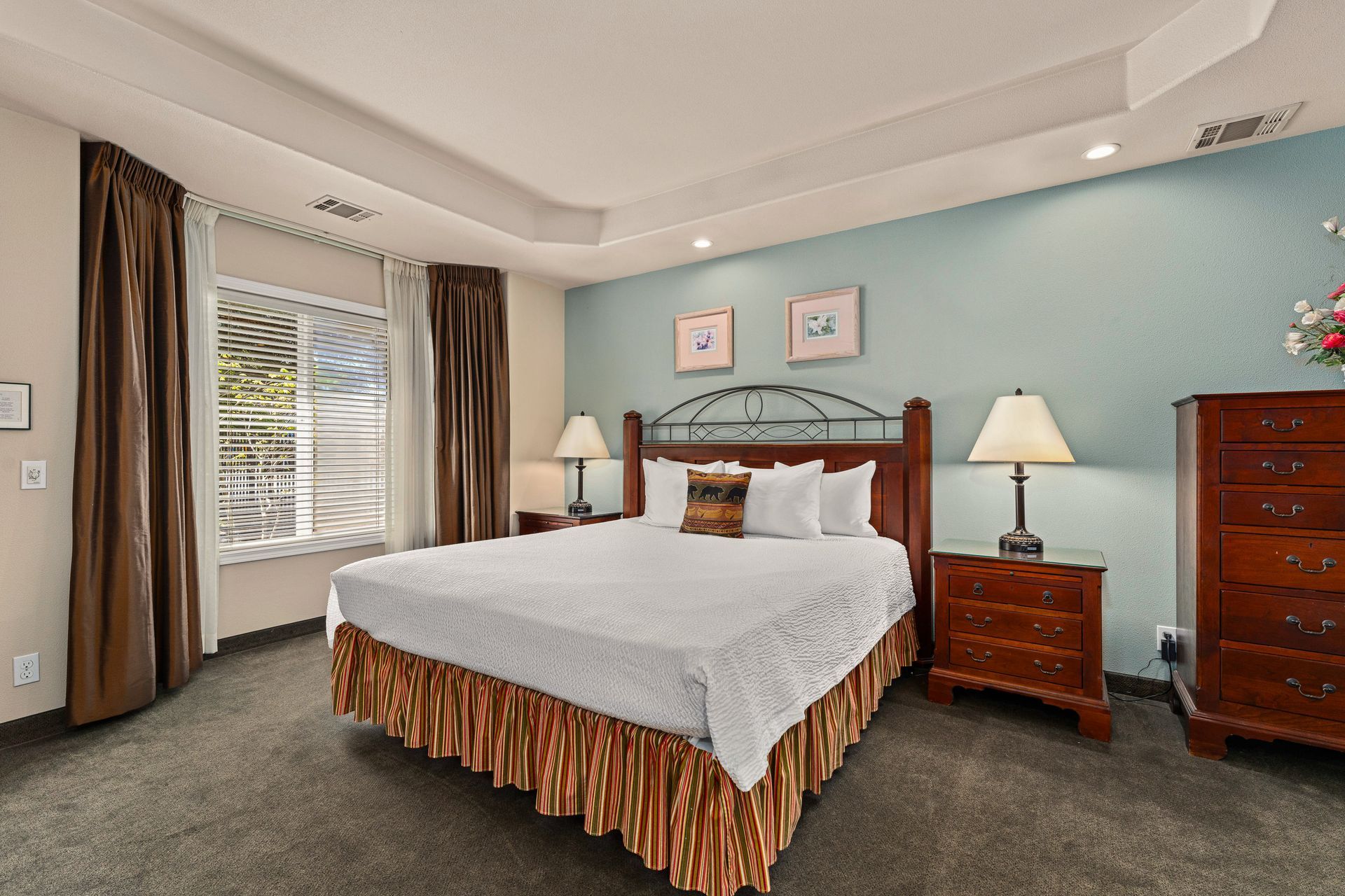 Bright bedroom with a large bed, bedside lamps, dresser, and window with curtains