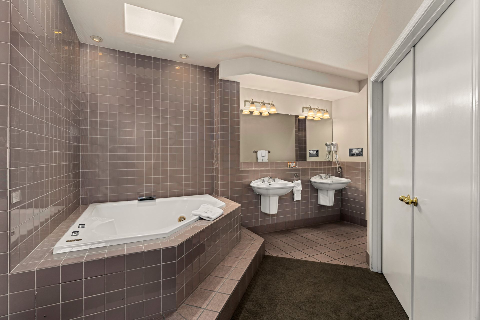 Bathroom with corner soaking tub, double vanity, pink tile walls, and sliding closet doors