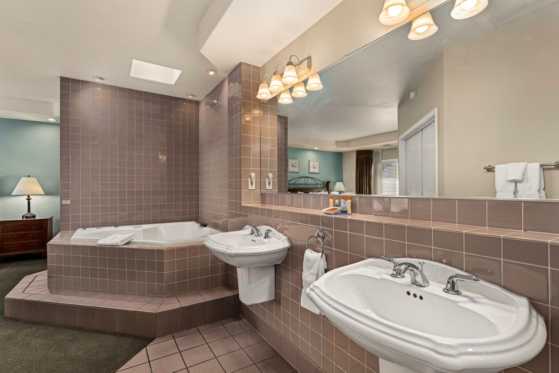 Spacious bathroom with pink tile, soaking tub, sink, large mirror, and vanity lights
