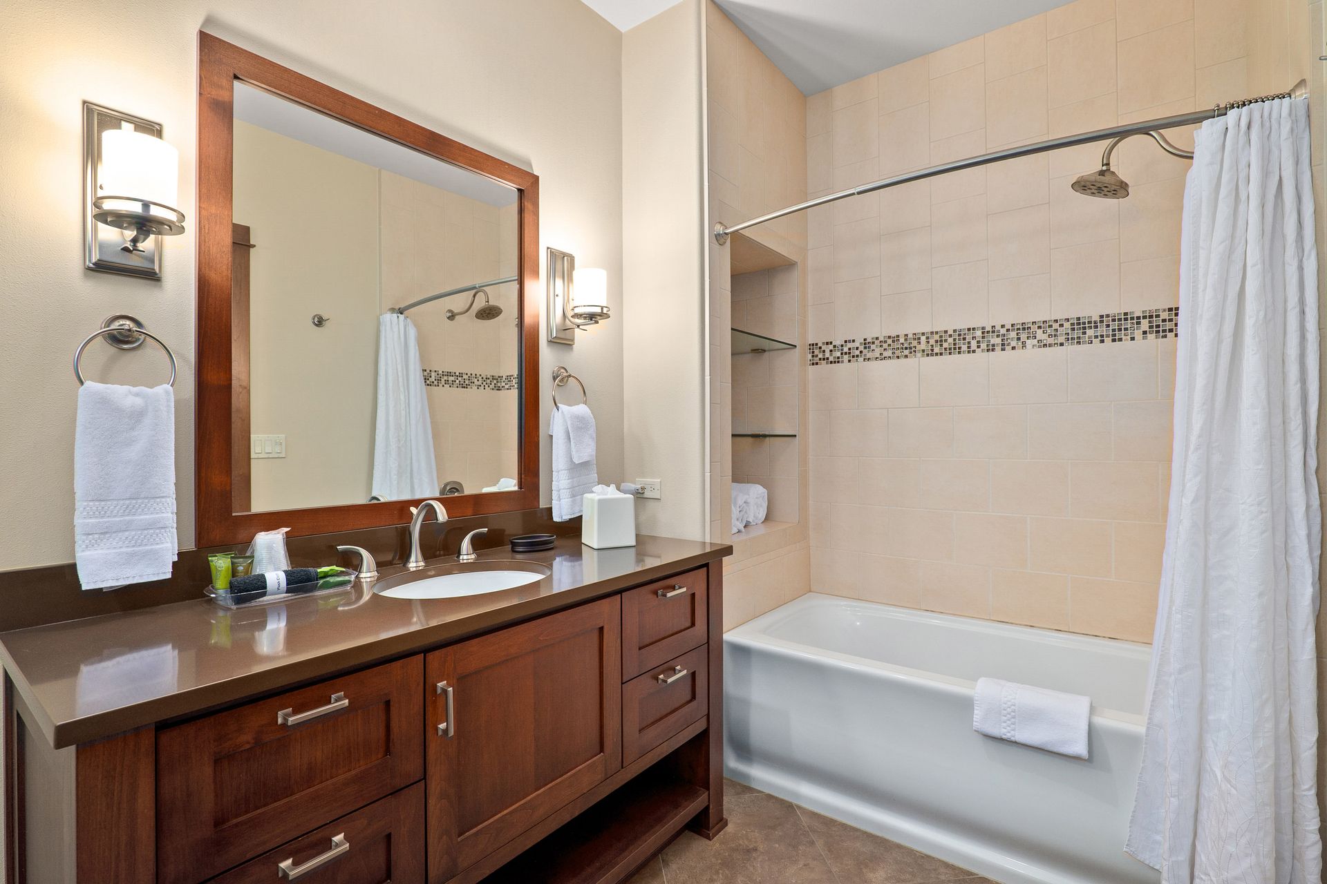 Bathroom with wood vanity, large mirror, and tub/shower with white curtain and beige tile.
