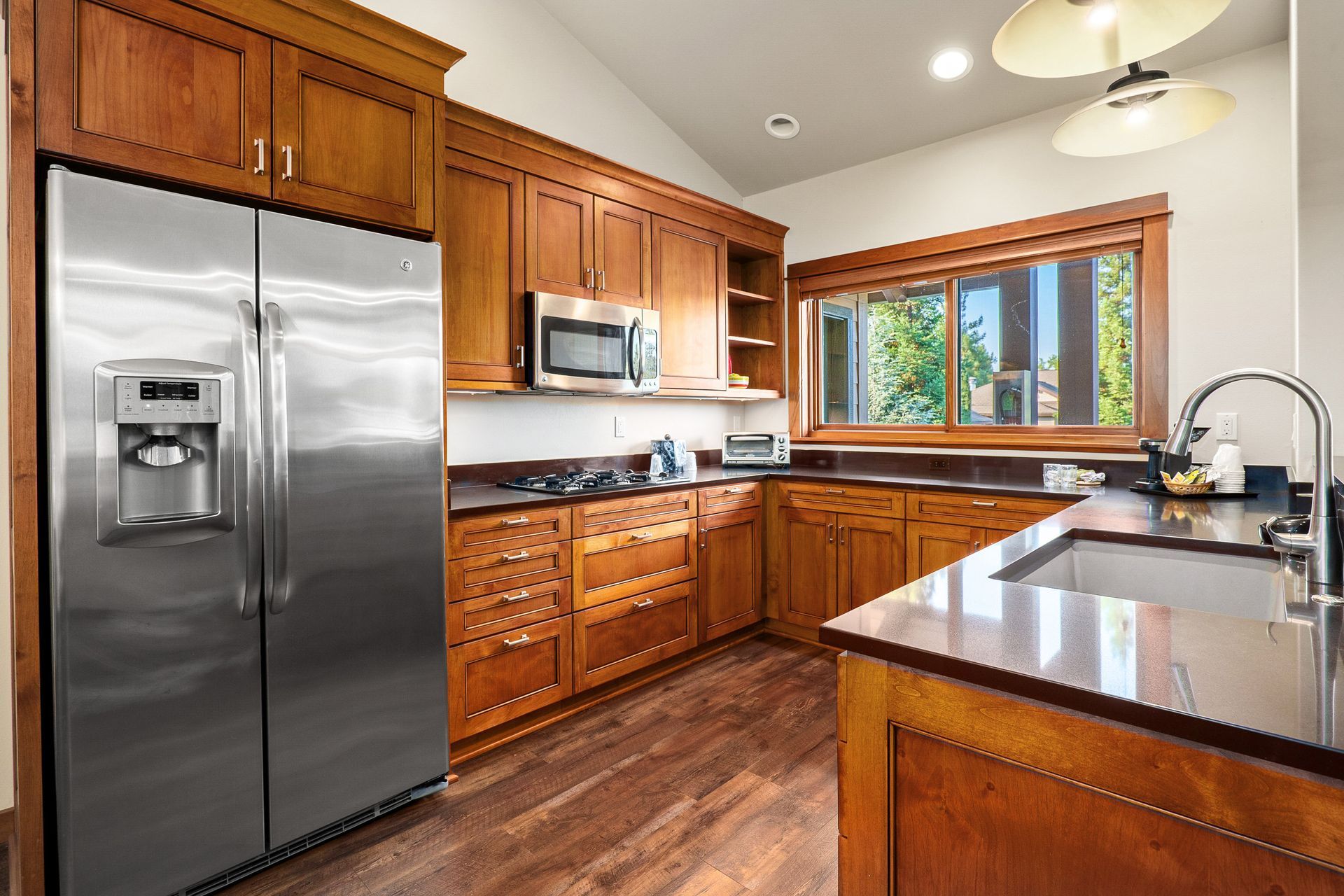 Modern kitchen with stainless steel appliances, wood cabinets, dark countertops, and a window over the sink