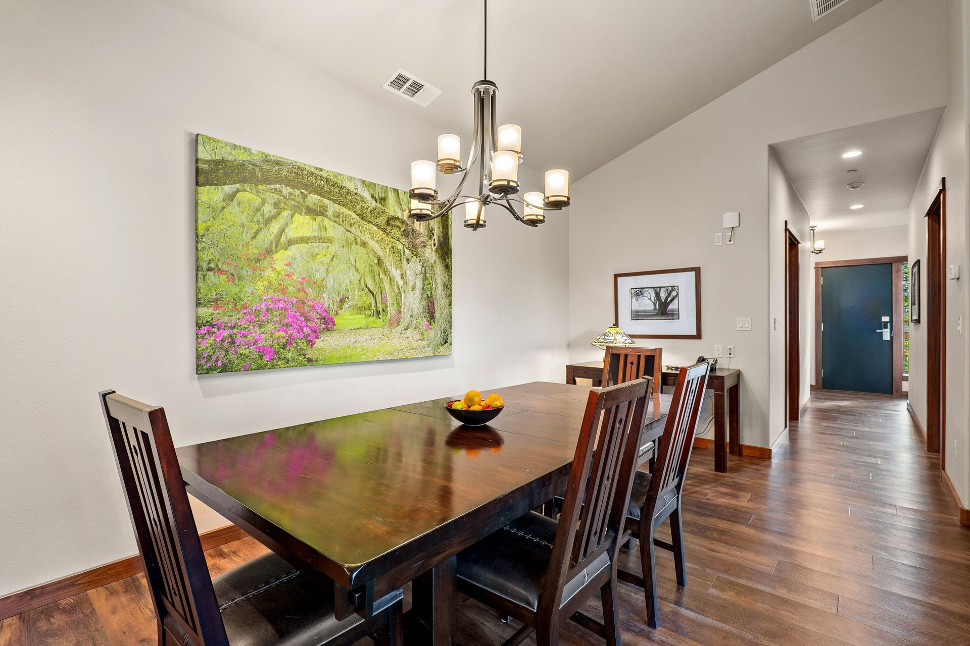 Dining room with dark wood table, chandelier, and landscape art on light walls.