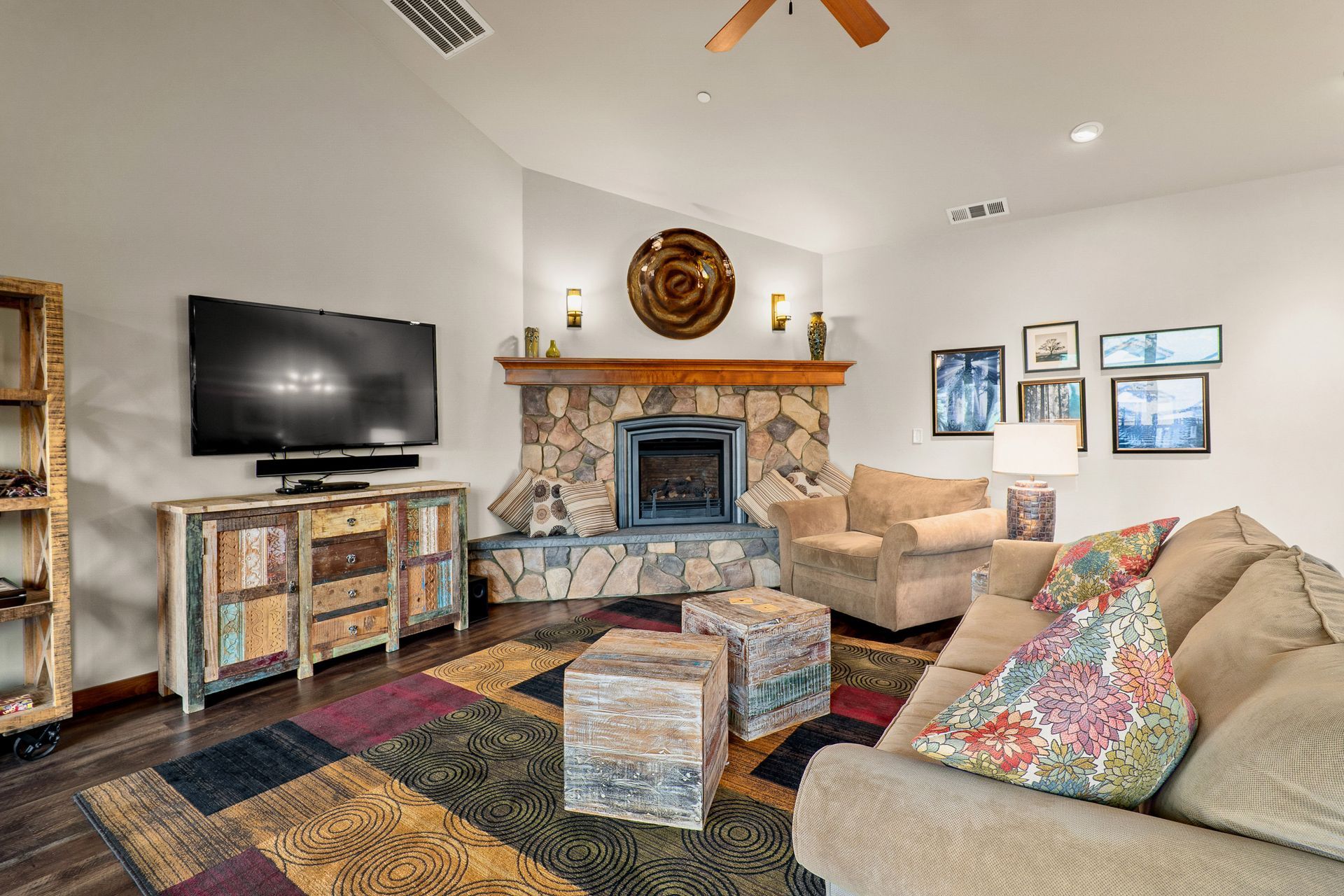 Cozy living room with stone fireplace, TV, patterned sofas, colorful rug, and framed wall art.