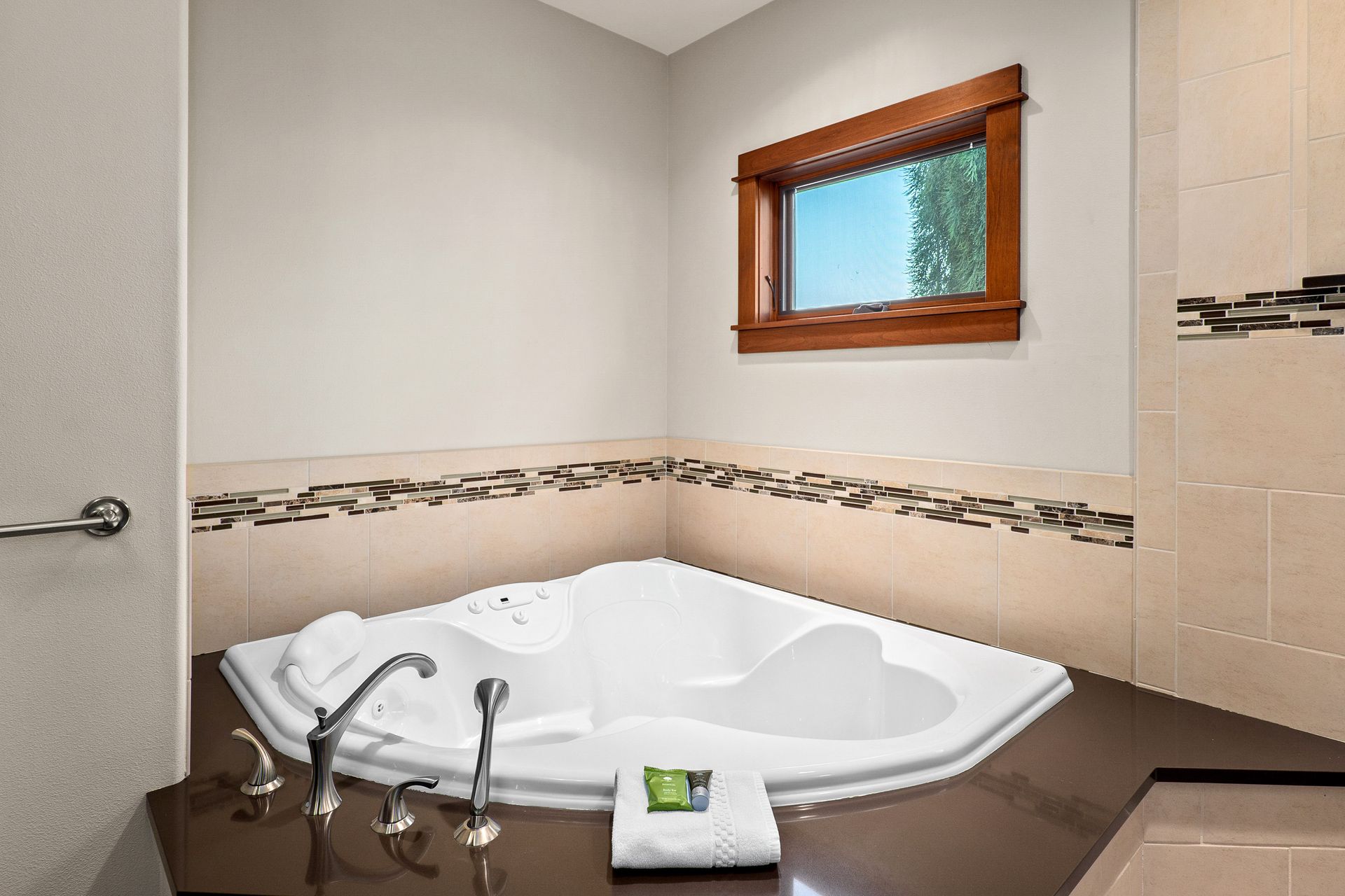 Bathroom with a white corner jetted tub, beige tile walls, and a small window above it